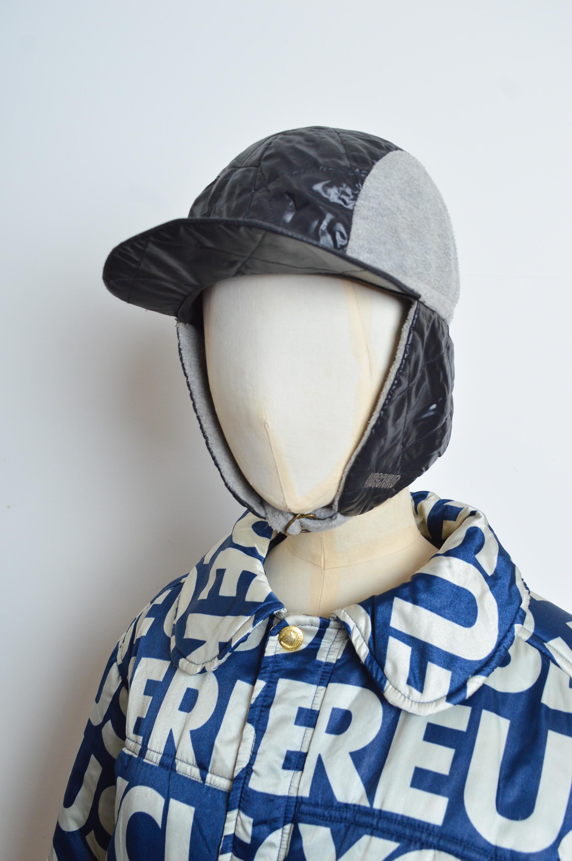 1990's MOSCHINO Jeans 'Rave' Cap crafted from Grey fleece with quilted nylon panels. 
The Trapper style Hat features a soft peak, elasticated reverse and fleece lined ear covers that can be worn tied under the chin or loose depending on desired