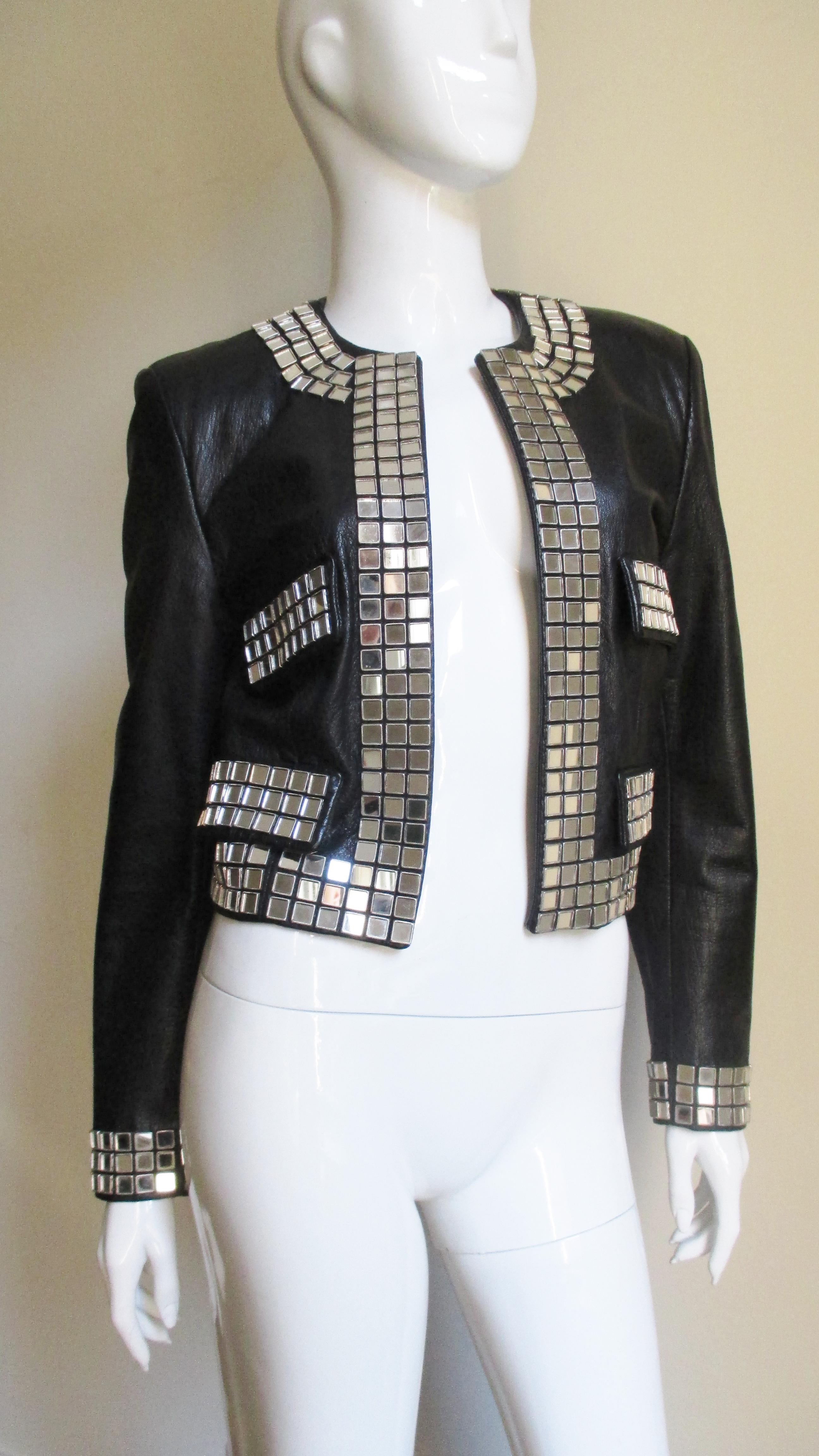 A fabulous black leather jacket from Moschino.  It is open in front with the pocket flaps, cuffs and jacket edges outlined in 3 rows of small square mirrors. It is fully lined and has lightly padded shoulders.  
Fits sizes Small, Medium.  Marked