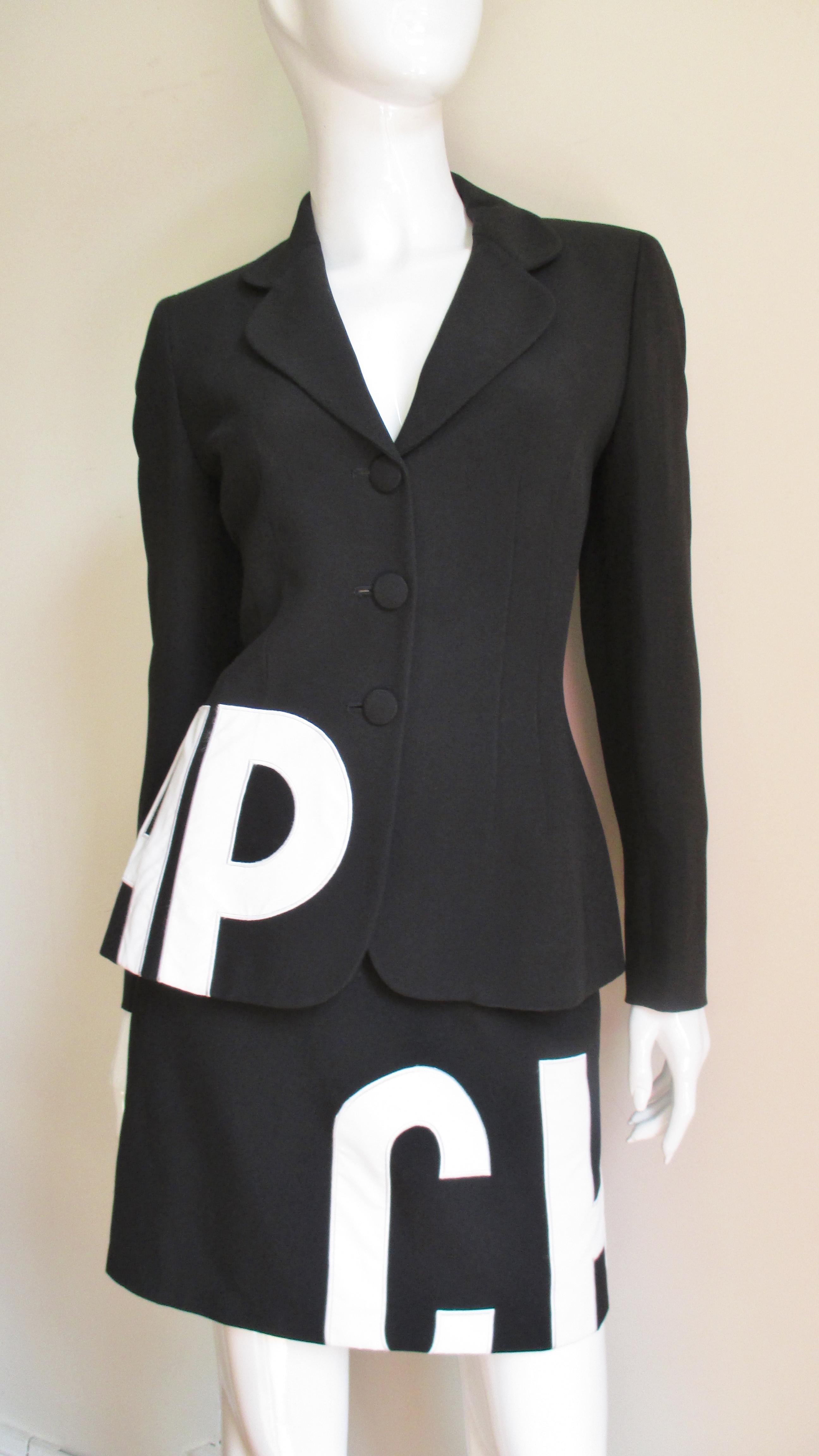 A fabulous skirt suit from Moschino in black and white. The blazer style jacket is semi fitted with rounded lapels and closing with 3 self covered buttons in front and three self covered buttons at each cuff.  It has the word CHEAP appliqued in