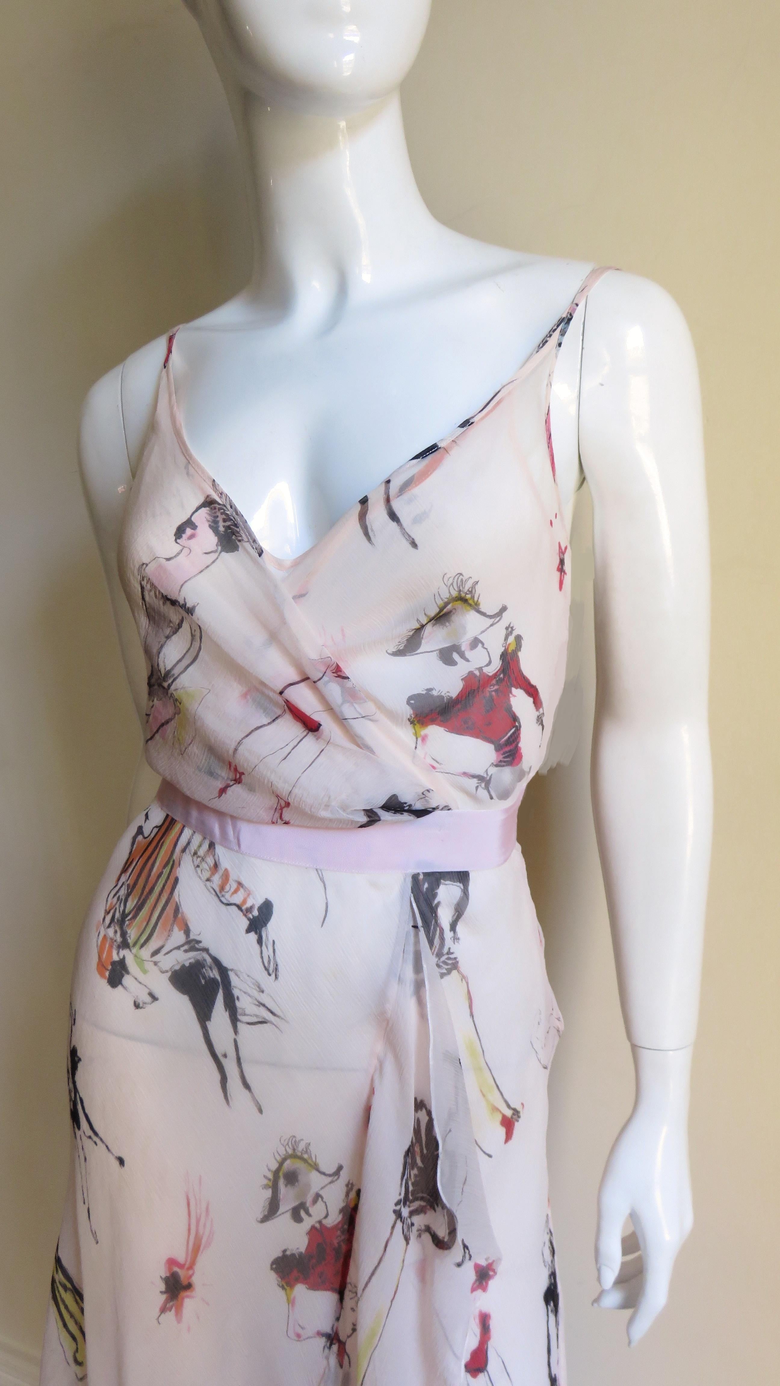 A pretty ethereal shell pink semi sheer silk dress and matching slip covered with sketches of people in costumes drawn in black, red and pink from Moschino. The dress has a wrap overlapping bodice with a matching pink grosgrain belt at the waist and