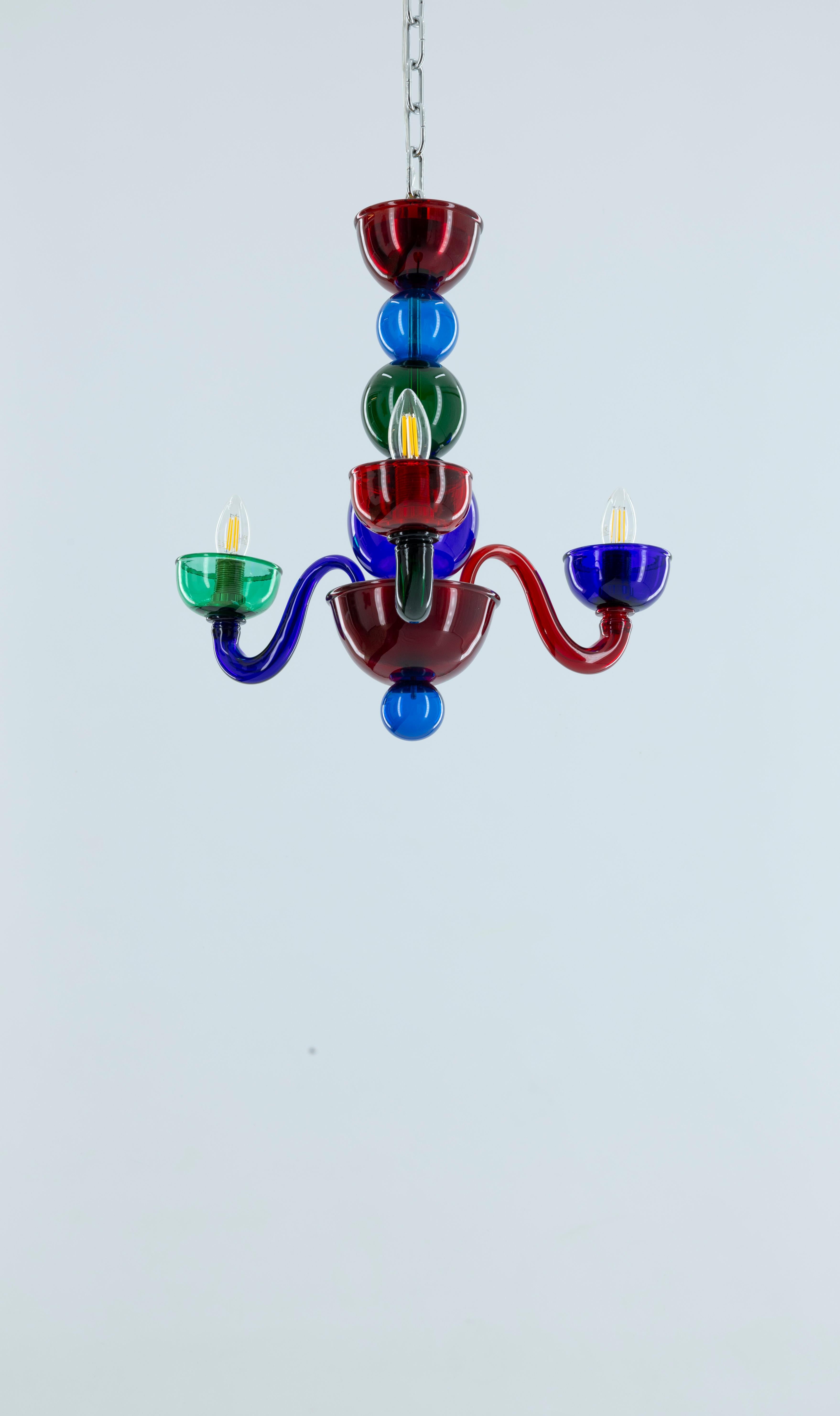 

This striking chandelier is an authentic Murano glass creation from the 1990s, showcasing a stylized spherical design. The piece is characterized by its rich ruby hue, complemented by a vibrant array of multicolored glass elements, all