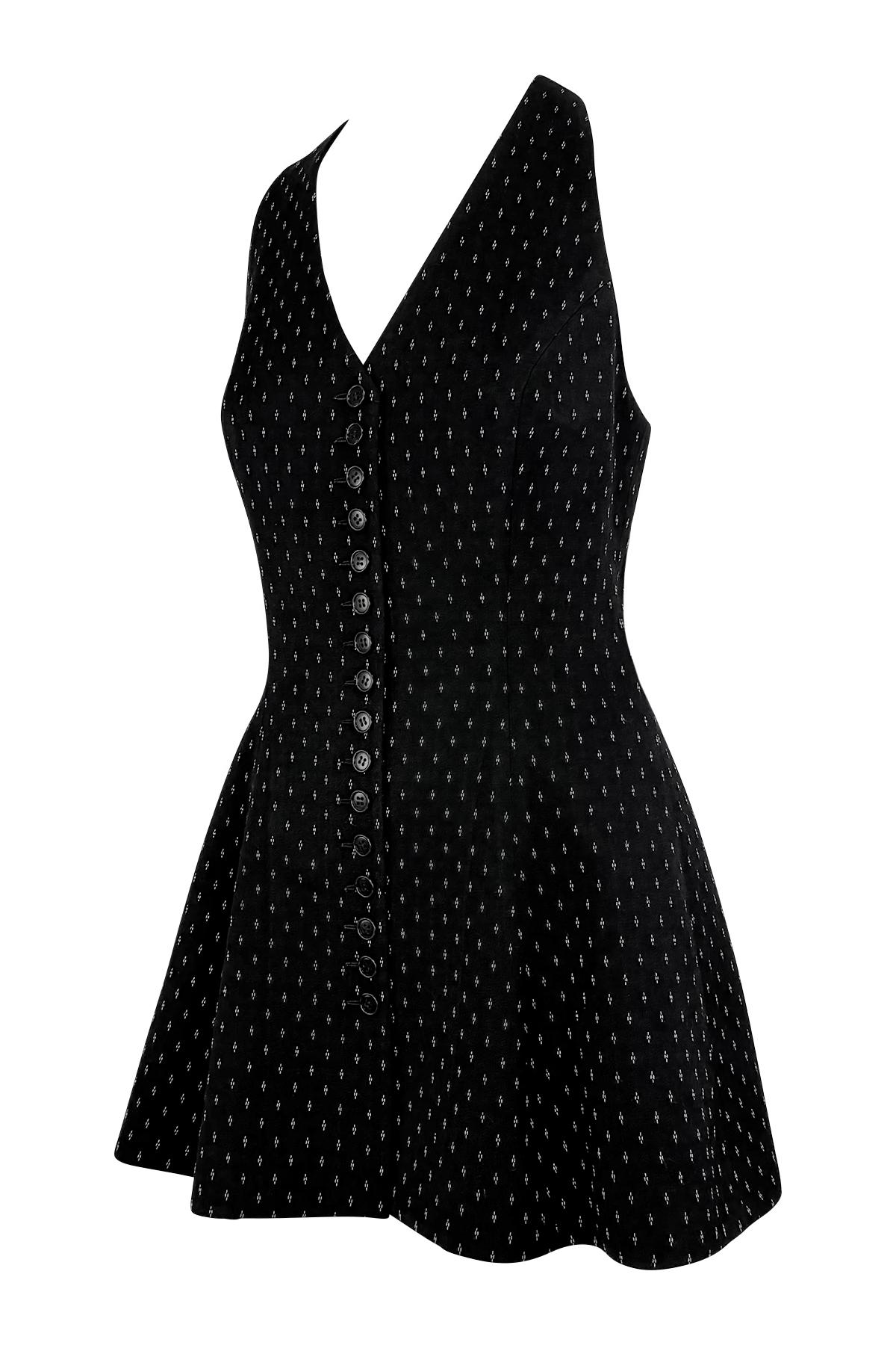 Este minivestido negro de Norma Kamali de los años 90 presenta una silueta sin mangas con detalles de puntadas blancas por toda la prenda. Diseñada con una falda acampanada y cierres de botones delanteros, la prenda ofrece un ajuste favorecedor y