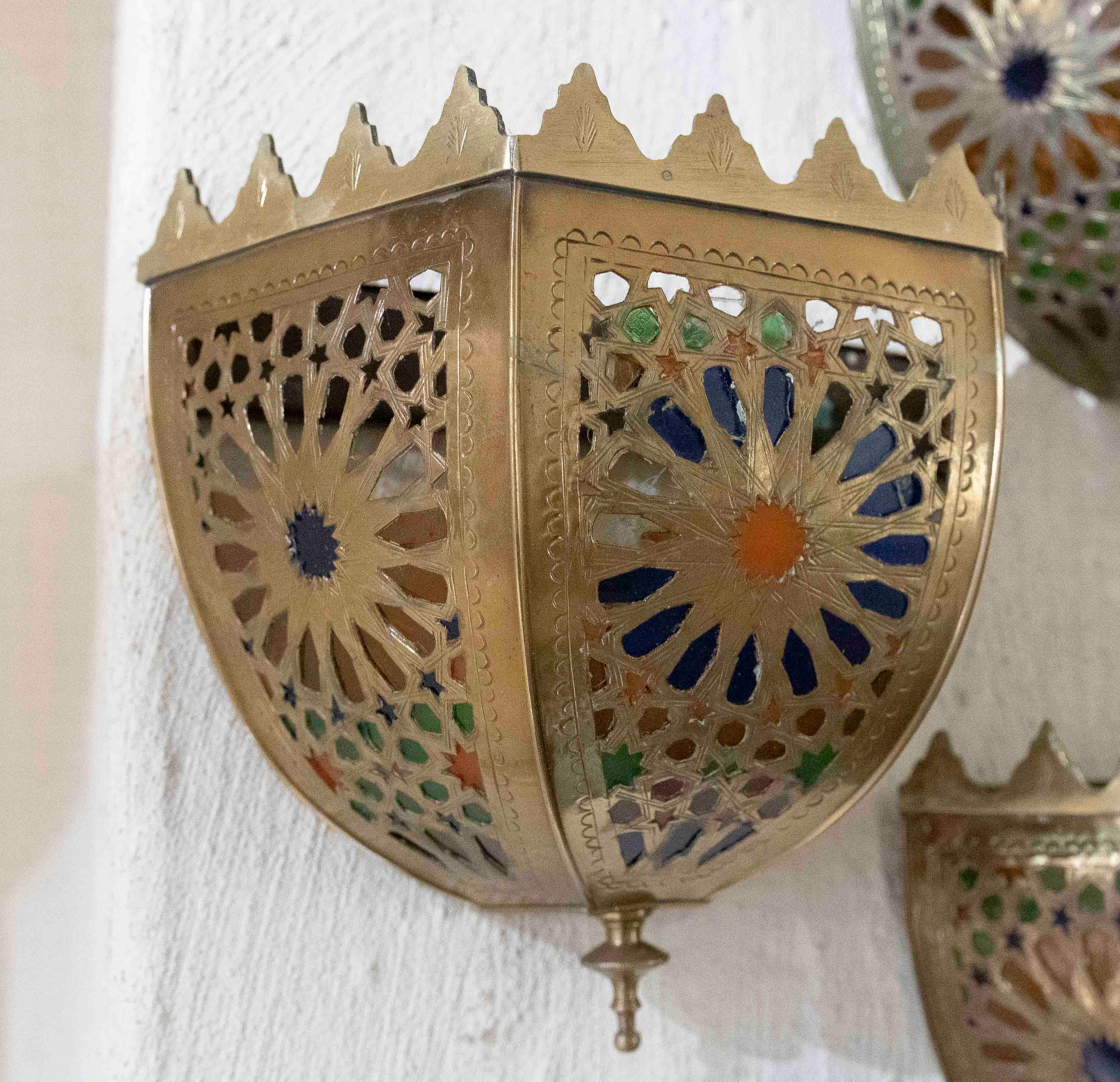 Exquisite pair of wall sconces made of brass with an openwork design that stands out for its handcrafted style and oriental touches. Each wall sconce is adorned with stained glass in shades of blue, green, orange and more, which filters the light