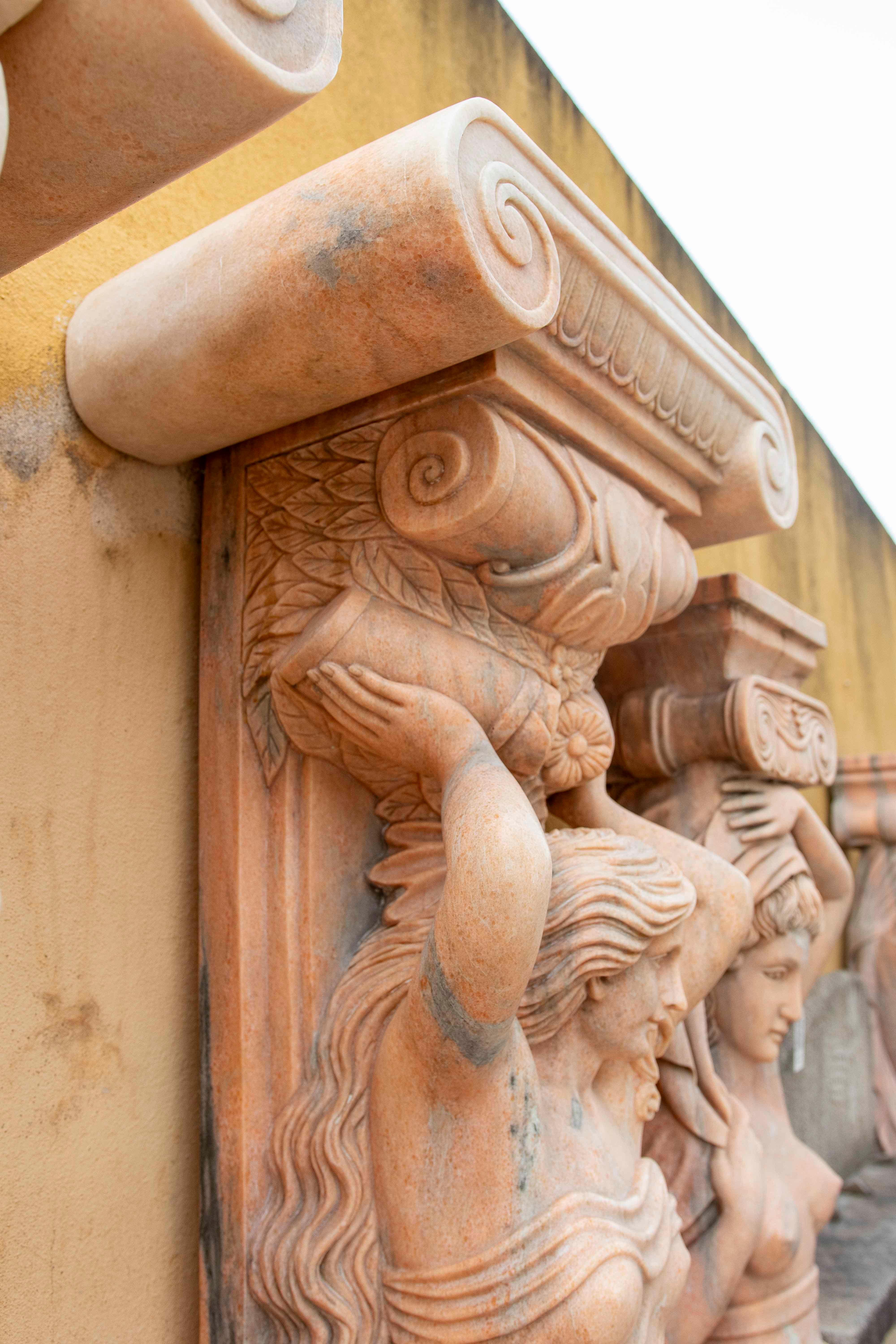 Prächtiges Paar handgeschnitzter Karyatiden aus Stein, inspiriert von der klassischen griechisch-römischen Architektur. Jede der zart gearbeiteten weiblichen Figuren hält ein reich verziertes ionisches Kapitell, zeigt fließende Falten in ihrem