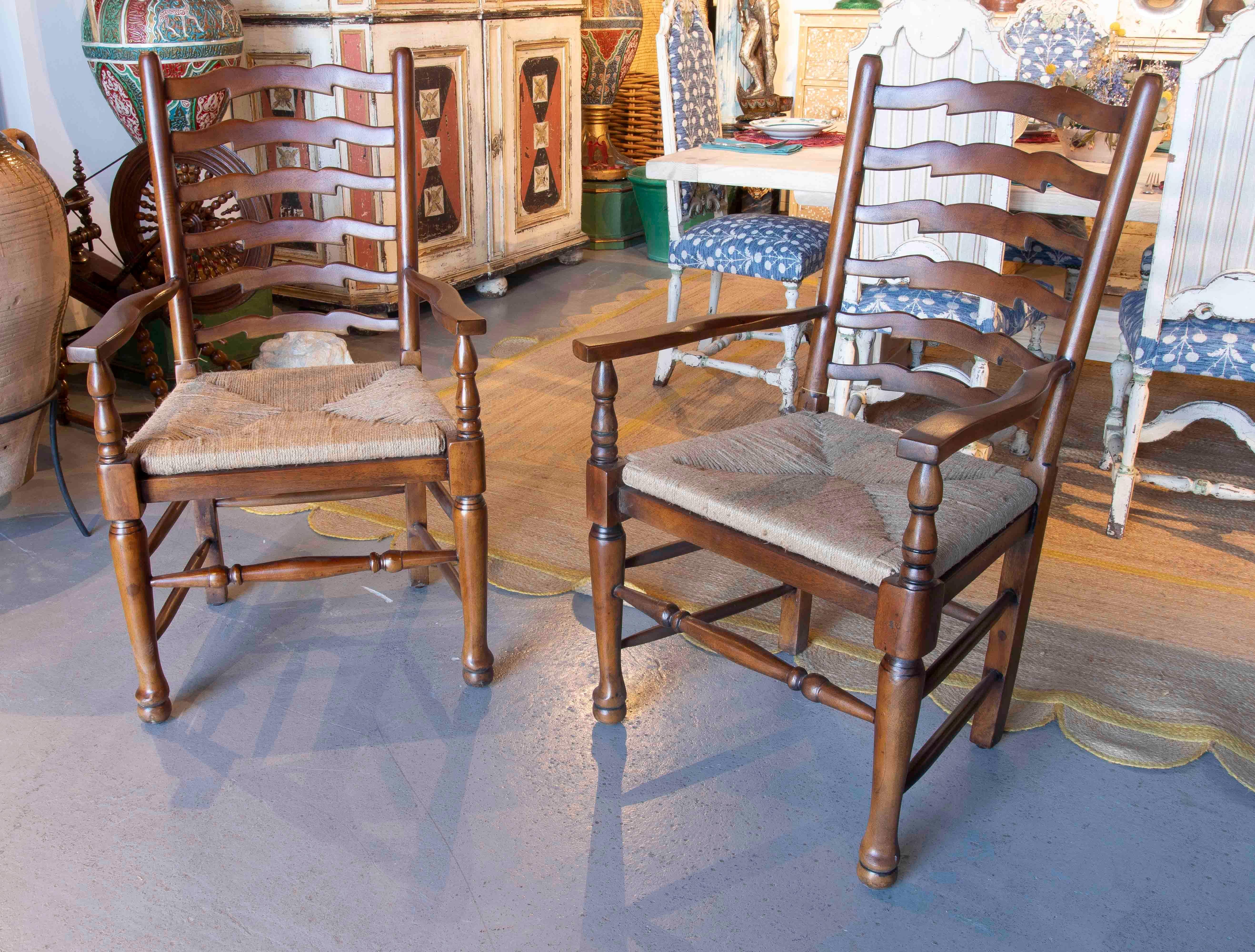 Encantadora pareja de sillas de comedor de roble con respaldo curvado de listones en forma de escalera y reposabrazos esculpidos. El asiento está tejido con fibra natural, una técnica tradicional que proporciona calidez y durabilidad, ideal para el