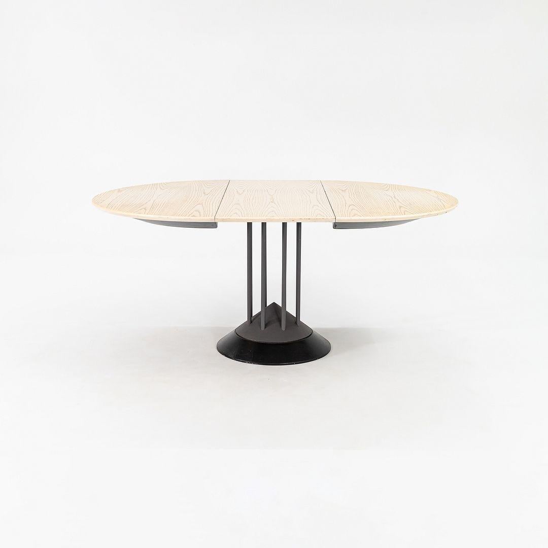 Se trata de una Mesa de Comedor Extensible Postmoderna, diseñada por Peter Maly para Tonon Italia en 1990. La base de la pieza presenta un motivo triangular, y tiene soportes tubulares centralizados de acero recubiertos de esmalte gris oscuro. La