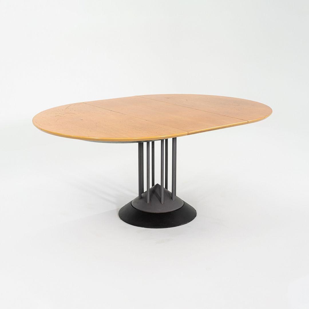 Se trata de una Mesa de Comedor Extensible Postmoderna, diseñada por Peter Maly para Tonon Italia en 1990. La base de la pieza presenta un motivo triangular, y tiene soportes tubulares centralizados de acero recubiertos de esmalte gris oscuro. La