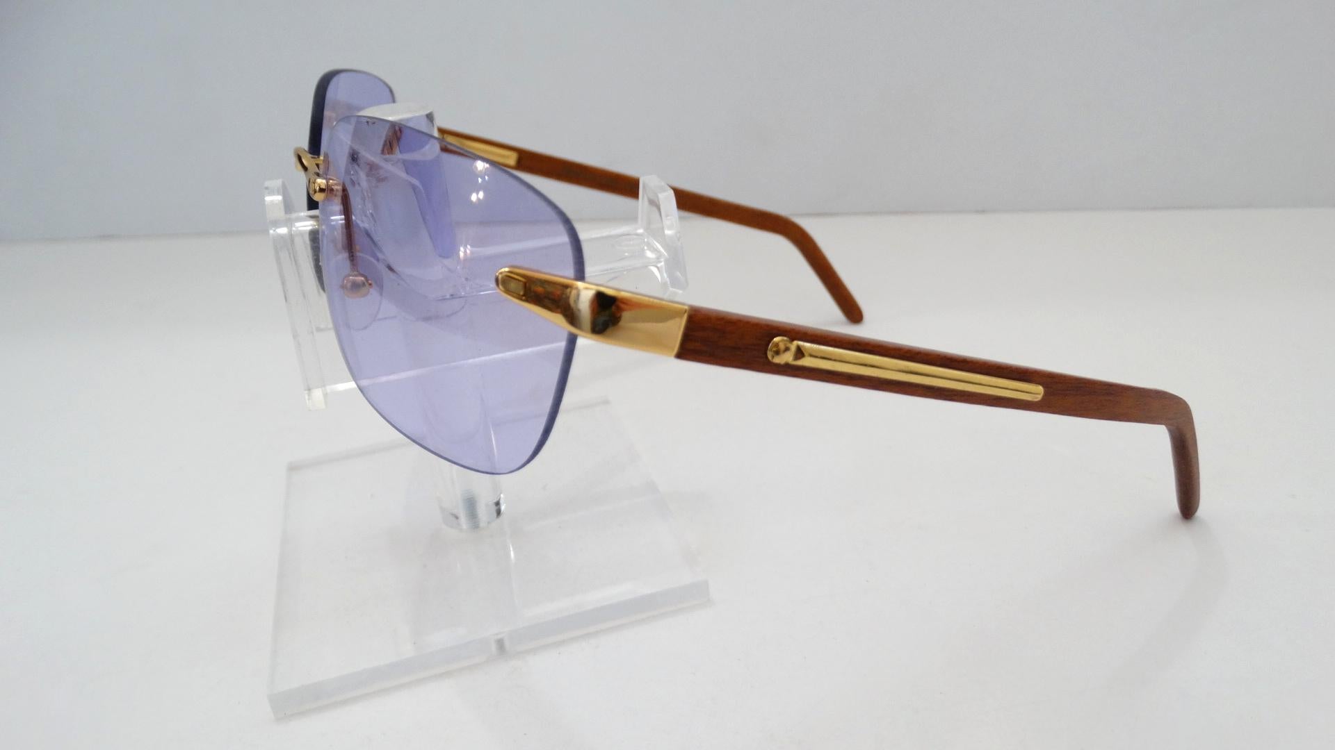 The Perfect Shade of Purple featured on these sunglasses. Circa 1990s, these dead stock Porta Romana rectangular sunglasses feature clear purple lens and gold hardware. The gold hardware sits on the lens and the light brown wood stain arms, features