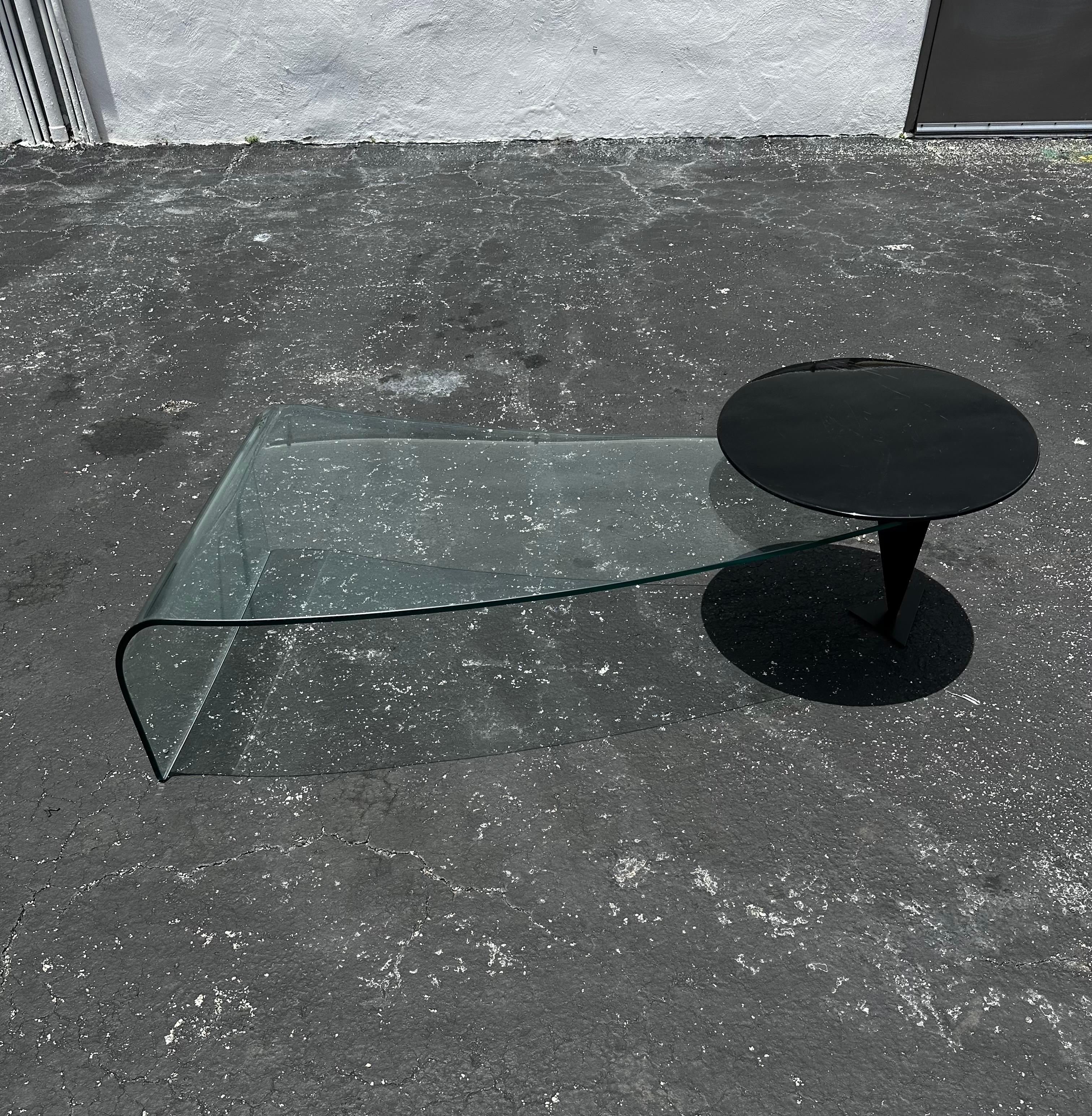 Table basse sculpturale postmoderne en verre à bord en cascade. Cette table étonnante se caractérise par un bord en cascade gracieux opposé à une extrémité gracieusement soutenue par une pyramide noire sur pied triangulaire. Un plateau pivotant