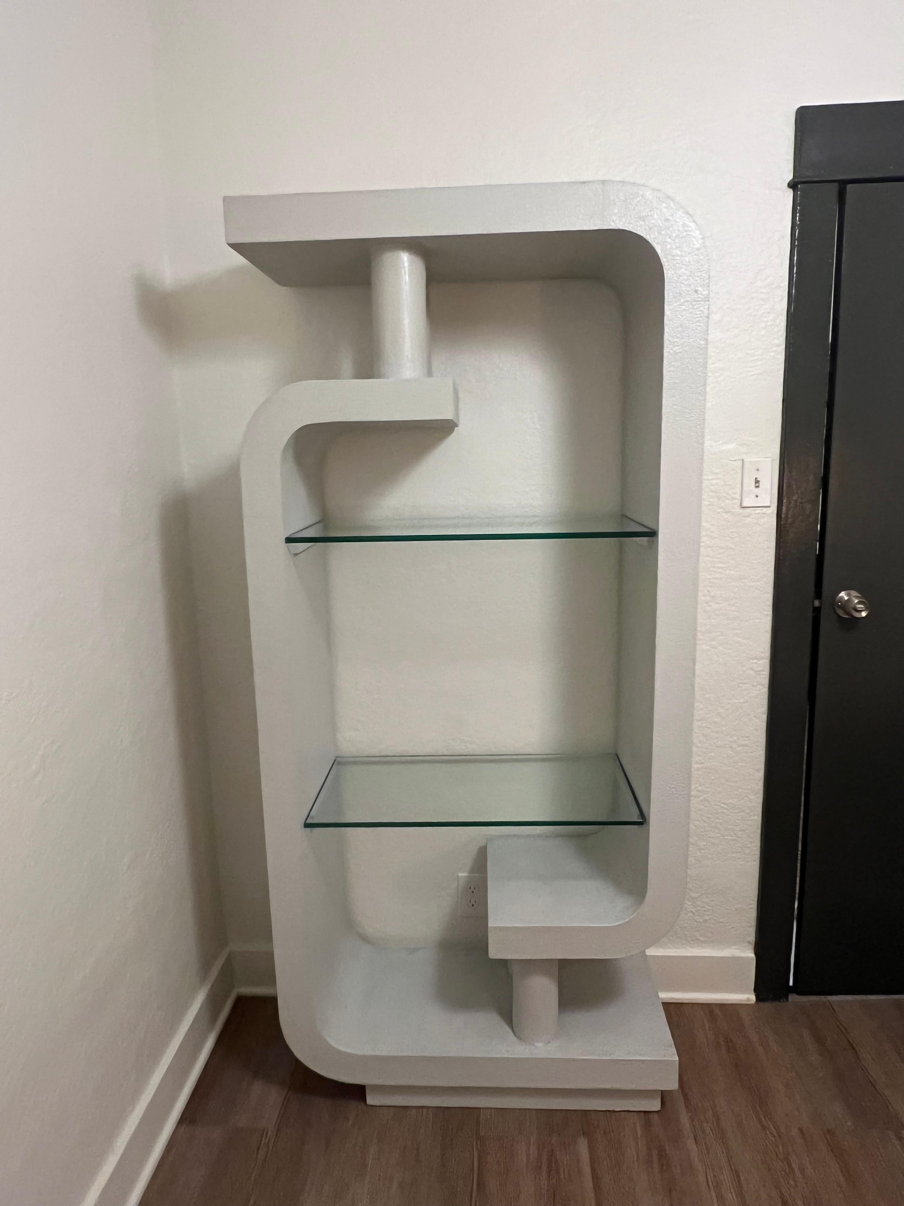 Classic postmodern sculptural etagere with two tempered glass shelves. Clean curves and lines sitting on a sleek plinth base. Made of fiberglass with a plaster texture on top of wood frame.  Light gray finish. Small chips on glass shelves- please