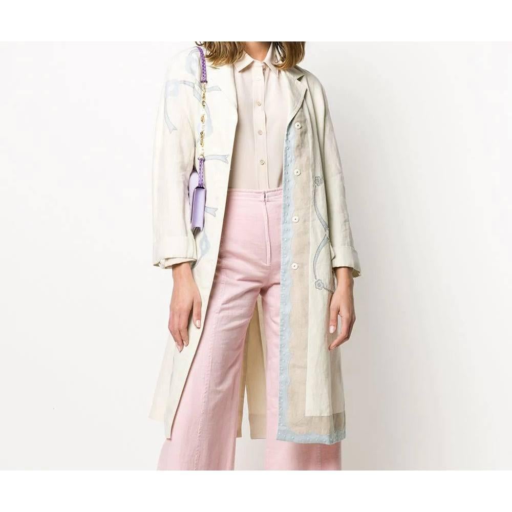 Cappotto medio-lungo di Prada in lino avorio con stampa azzurra, con colletto con revers classici, maniche lunghe, chiusura frontale nascosta con bottoni automatici, due tasche anteriori a filetto con patta. Sul retro presenta una profonda