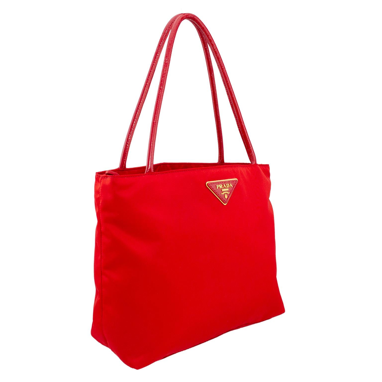 Add the perfect pop of color to any look with this beautiful red Prada nylon medium tote bag from the 1990s. Simple and classic shape with triangular Prada logo and red patent leather handles. Two large open interior compartments divided by a third