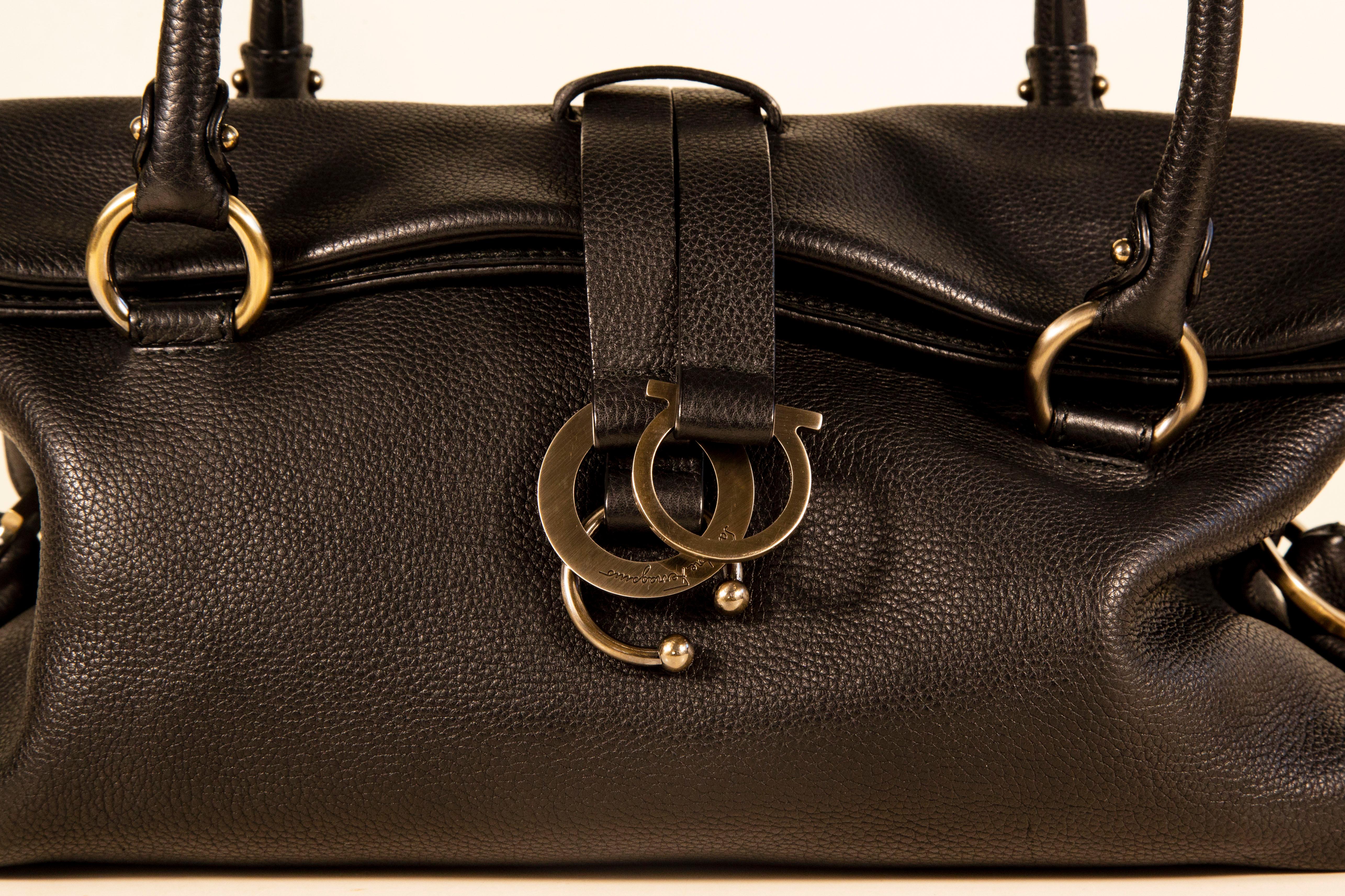 Un sac à bandoulière/à poignée supérieure de Salvatore Ferragamo. Le sac est en cuir noir avec des accessoires en acier. L'intérieur est doublé de tissu synthétique noir. A côté du compartiment principal, il y a trois poches latérales dont l'une est