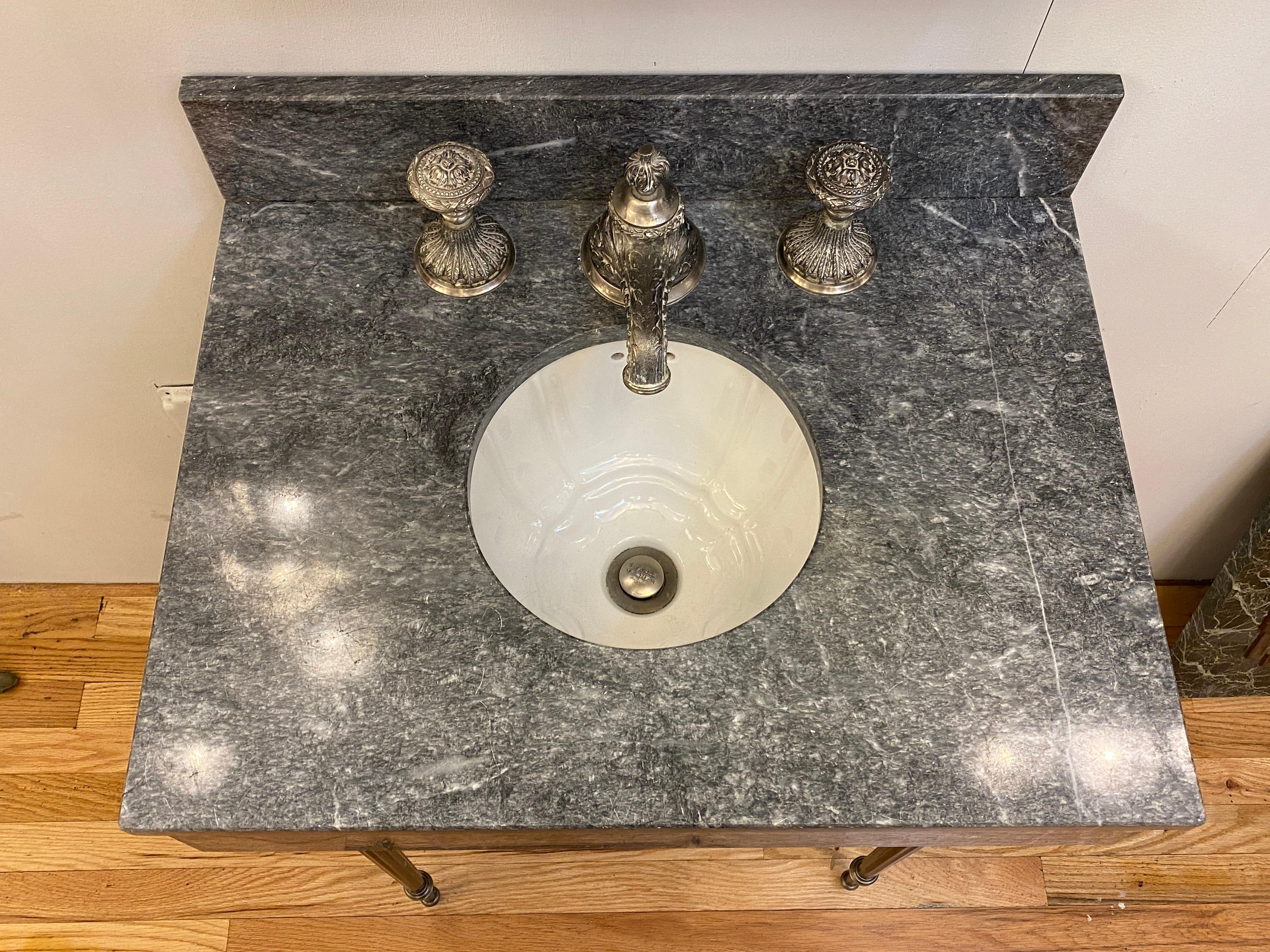 1990s petite gray marble console sink by Sherle Wagner. Showing a scalloped white ceramic sink basin and reeded style legs. Also has their Louis Petite knob faucet set in pewter. From a Park Ave apartment in Manhattan. This can be seen at our 333