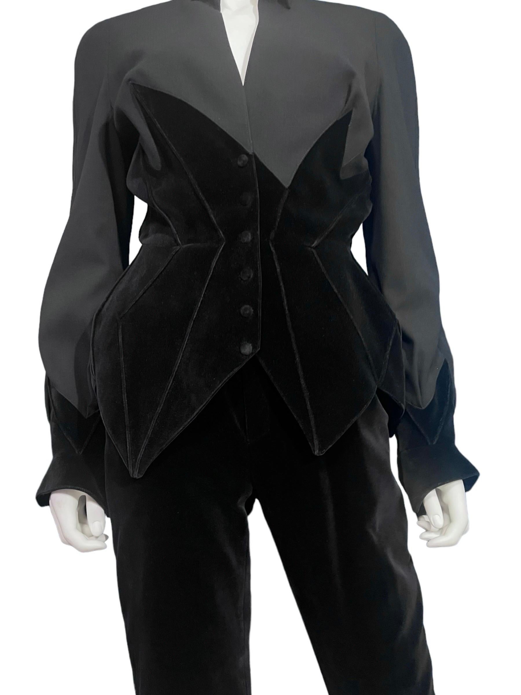 Exceptional Thierry Mugler 1990's black wool and velvet two piece pantsuit ensemble. This vintage pantsuit features a strong shoulder black wool jacket with striking contrasting velvet trim and matching velvet pants.
The jacket has jagged edge