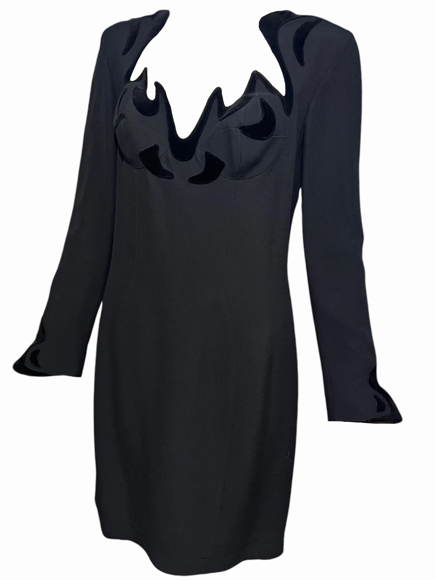 Abito drammatico in velluto nero di Thierry Mugler. Presenta un design con ritagli frastagliati e velluto nero floccato intorno al busto, alla scollatura e ai polsini. Questo abito ha le spalle padellate e il reggiseno incorporato che creano la