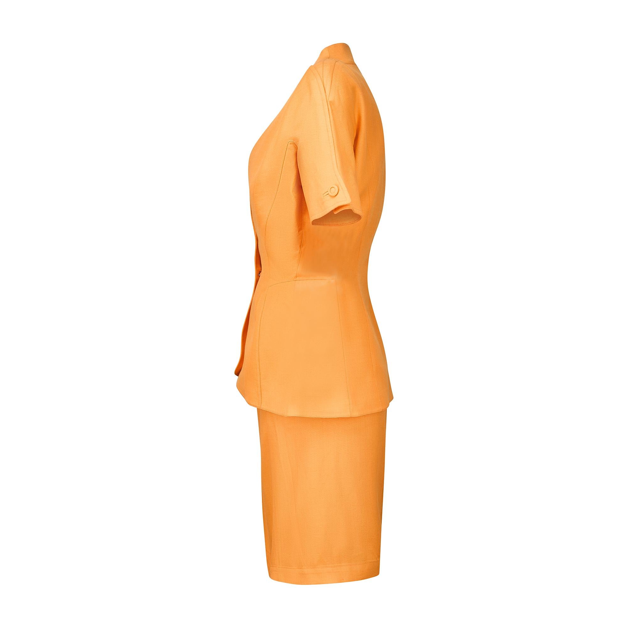 Questo tailleur con gonna in lino arancione di Thierry Mugler degli anni '90 è realizzato su misura secondo i contorni definiti che caratterizzavano il lavoro dello stilista in quell'epoca. La giacca del tailleur a forma di peplo con padiglioni
