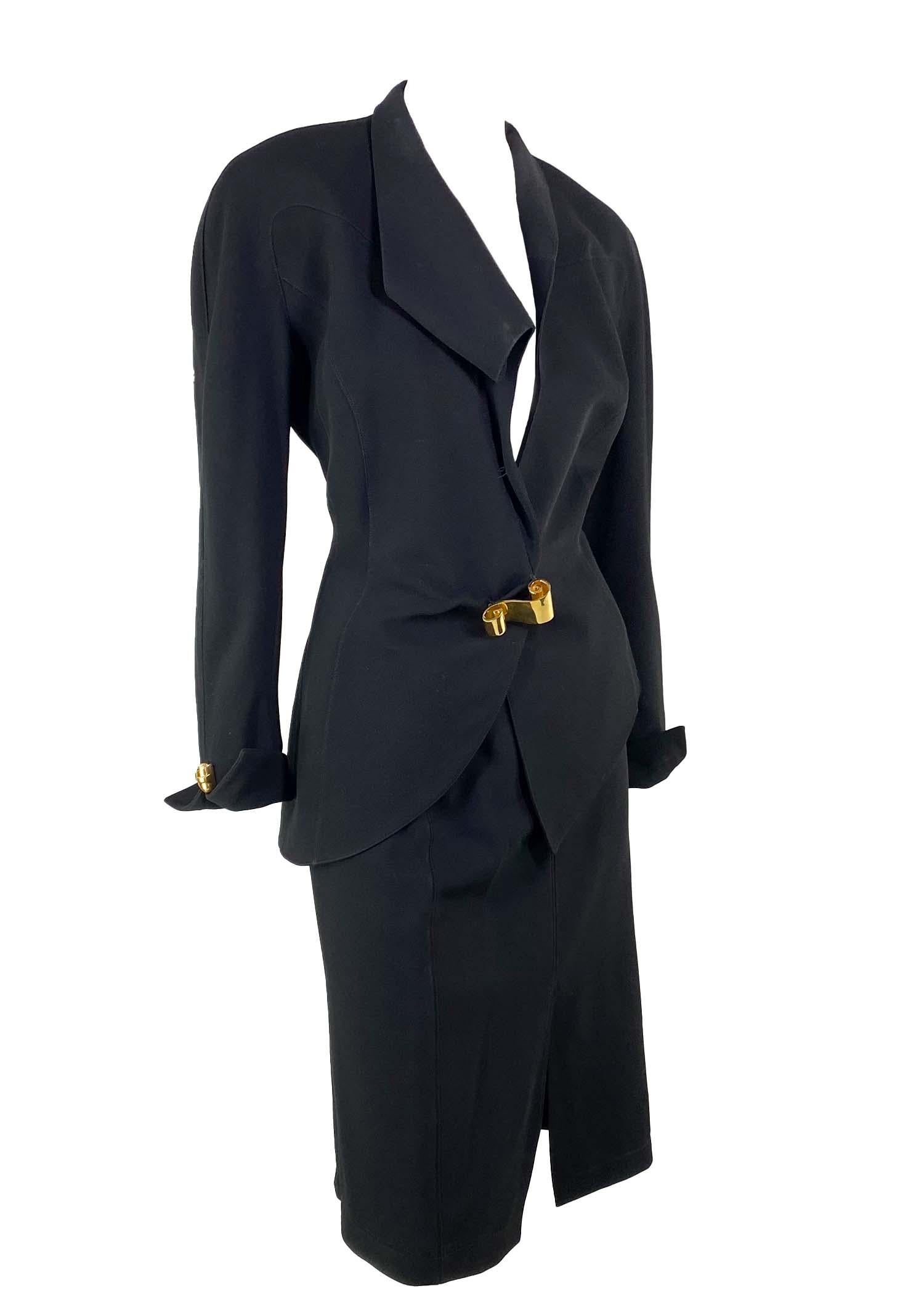Presenting a sculptural Thierry Mugler skirt suit, designed by Manfred Mugler. From the 1990s, this suit features masterful design and tailoring. The blazer features a sculptural curved lapel with gold metal scroll closures at the front of the