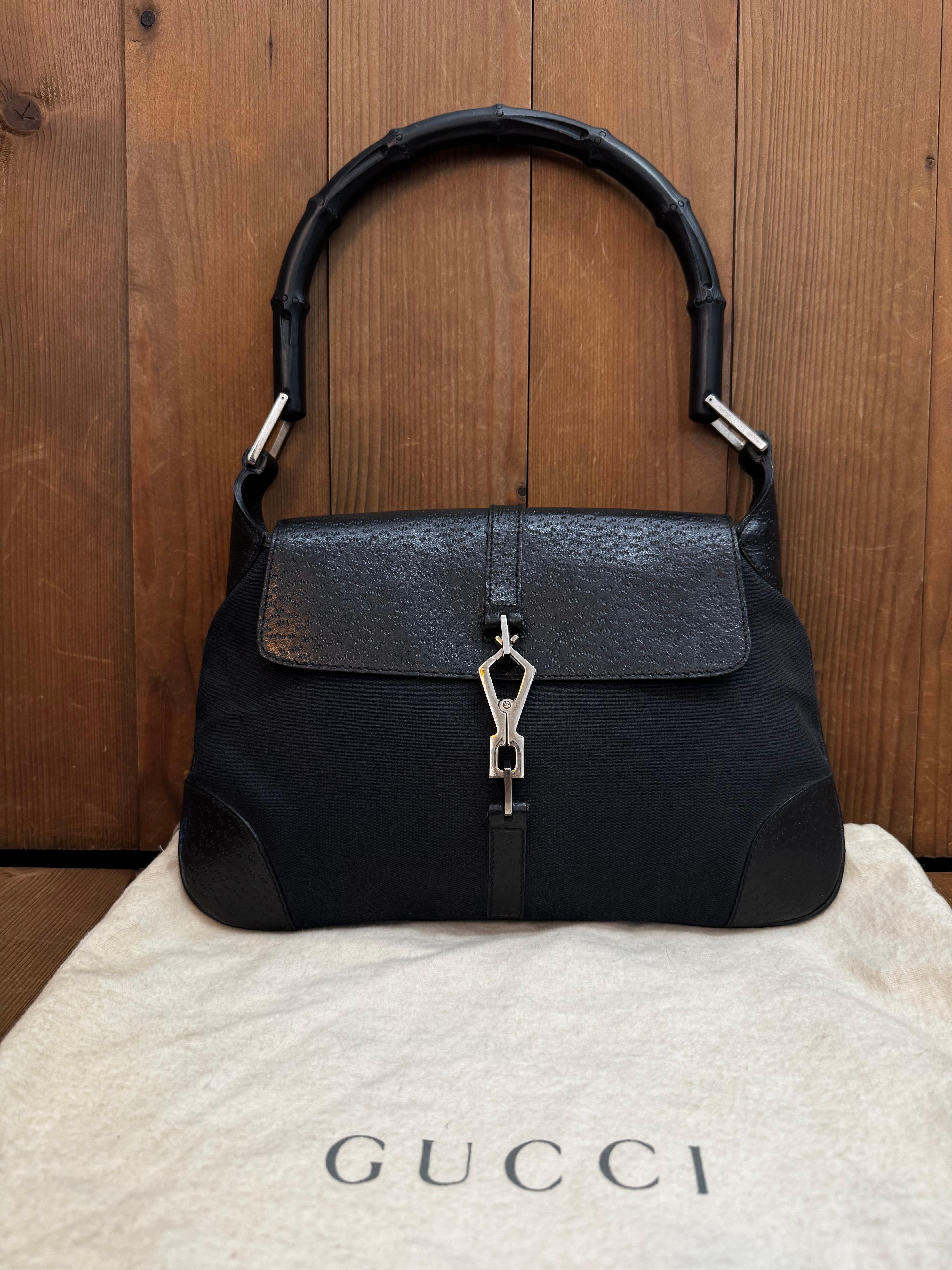 This Tom Ford era’s GUCCI Jackie Bamboo hobo bag is crafted of black canvas trimmed with pigskin leather in black featuring silver toned hardware and a black resin bamboo handle. Front flap lobster claw closure opens to a black G monogram jacquard