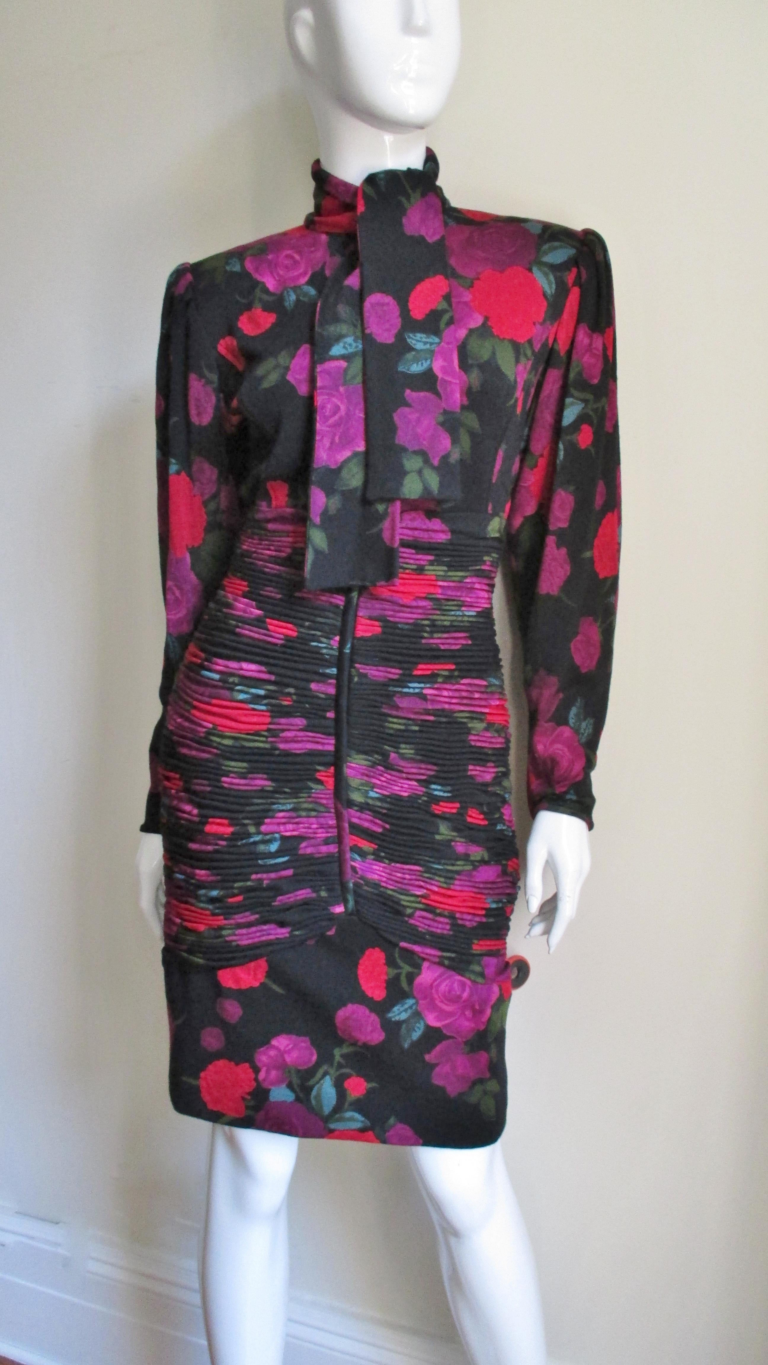 A gorgeous fine wool jersey fitted dress from Emanuel Ungaro with purple and red flowers popping against the black background. It has a tie neckline, full sleeves with zipper cuffs and beautifully intricate horizontal ruching around the dress