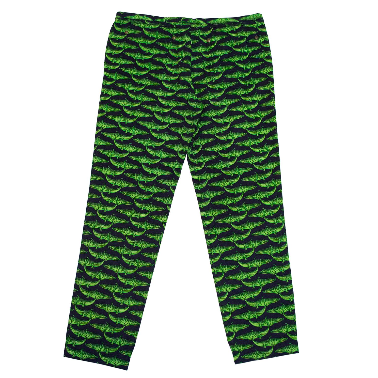 1990s Versace jeans. Black with an all over green alligator print. left leg is further detailed with contrasting blue  and tropical palms trees. Pattern is a tribute to Miami with the alligators and palm trees, where the Versace Mansion is located.
