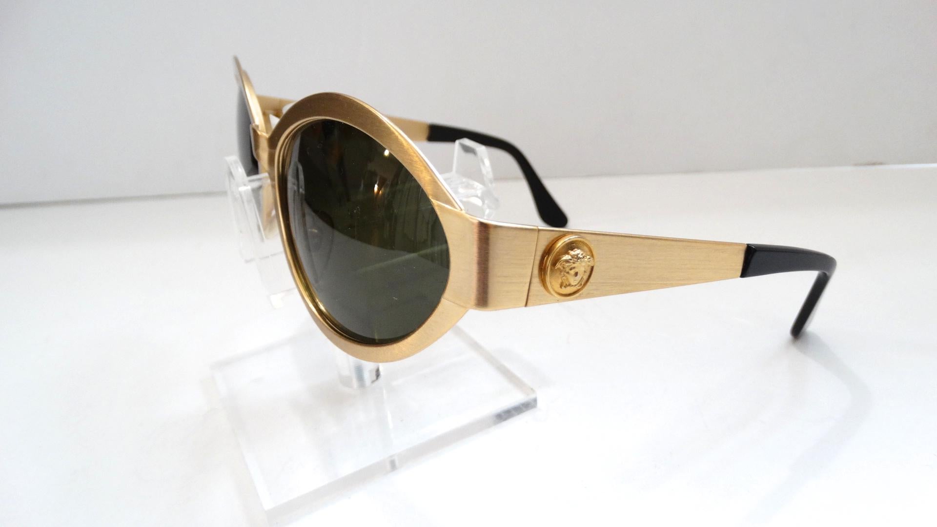 All Eyes On You While Wearing These Killer Versace Sunglasses Circa 1990s! A dead stock treasure, these sunnies are a wide oval shape and feature a matte gold metal frame. Includes dark black lenses and a gold Medusa head emblem on each arm. A true