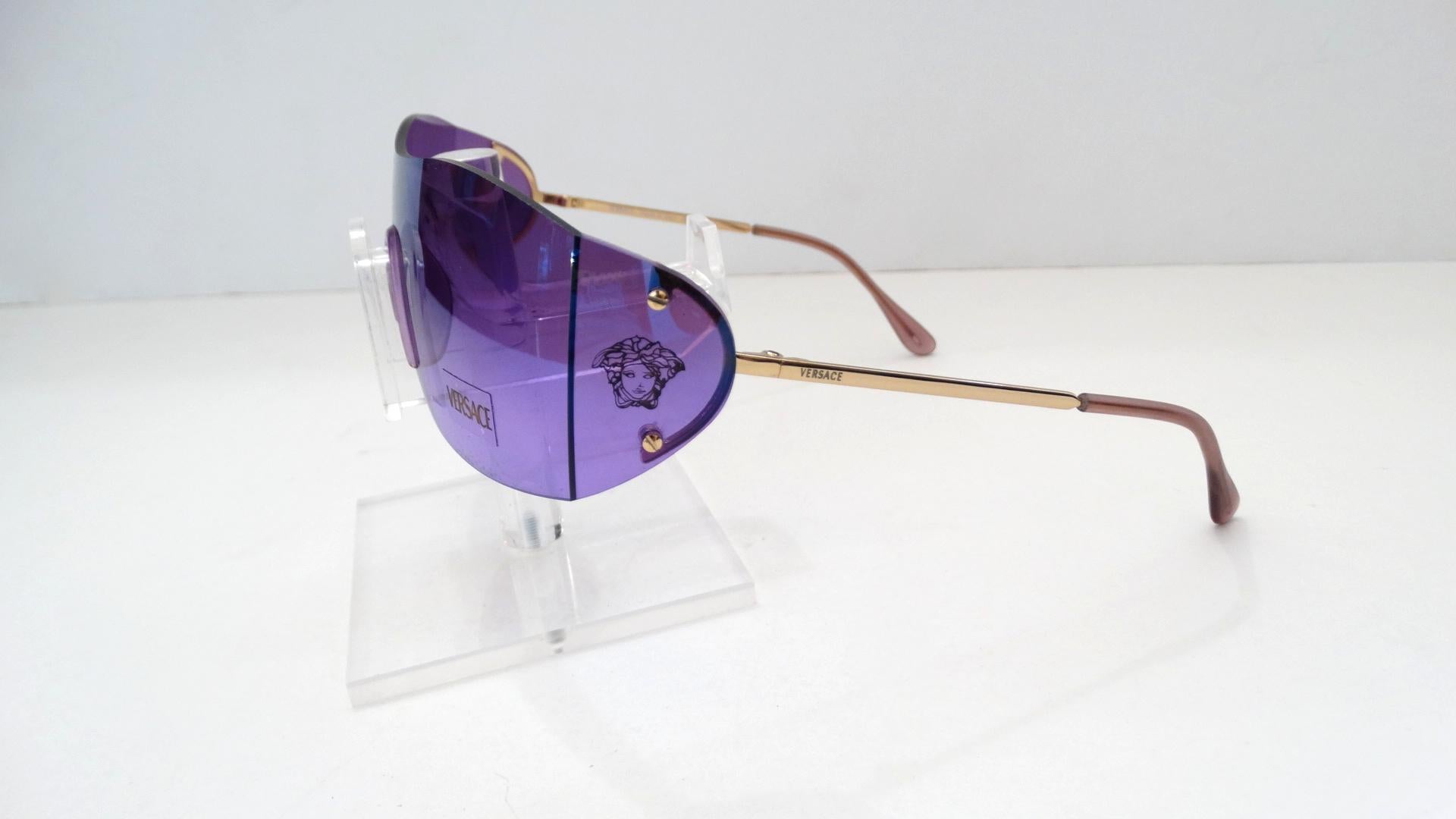 The Perfect Pair Of Sunglasses For Your Street Chic Street Style! Circa 1990s, these dead stock Versace shield sunglasses feature purple iridescent lenses, silver hardware and light purple arm covers. The side of the sunglasses are stamped with the