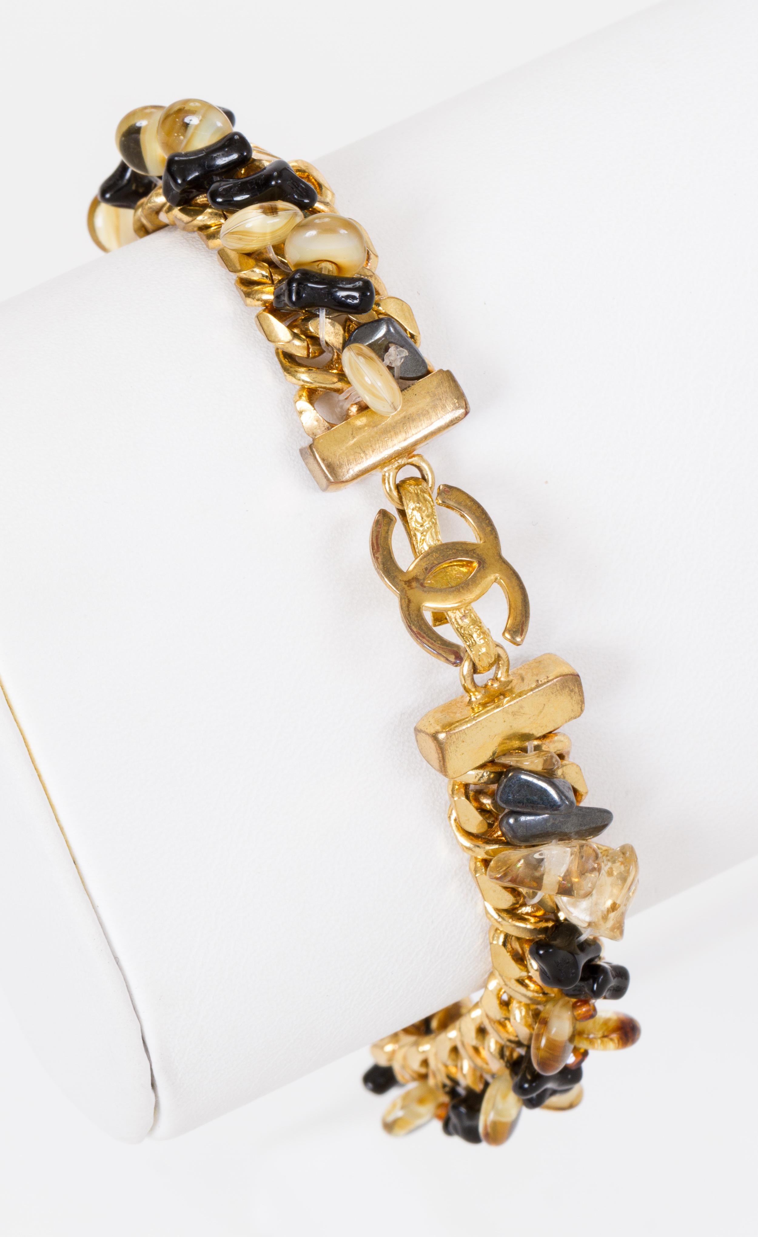Bracelet Chanel en métal doré orné de perles de verre brunes et noires. Collection printemps 99. Livré avec une pochette originale. Usure mineure.