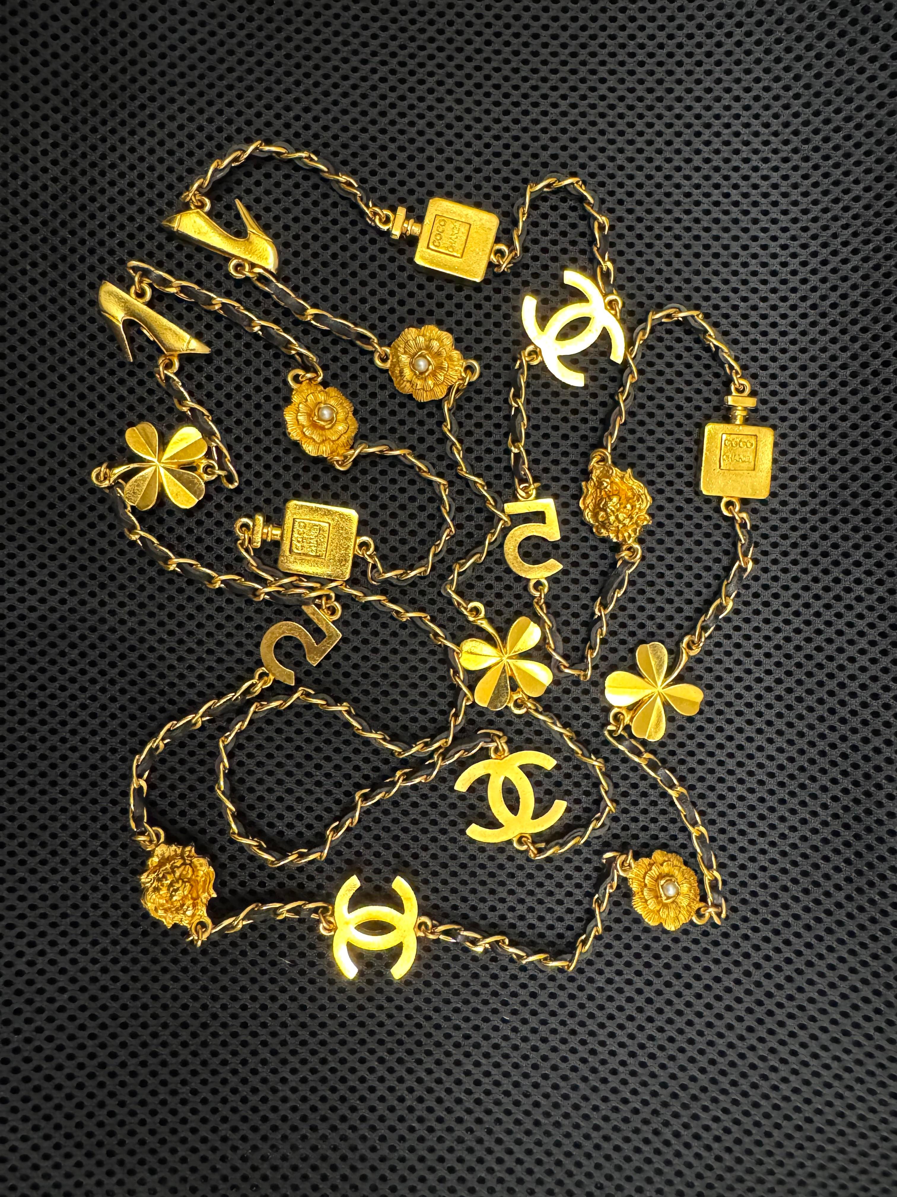 Questa collana a catena lunga CHANEL vintage del 1996 è realizzata con una catena dorata intrecciata con pelle nera con 18 motivi iconici CC Camellia No.5 Clover Lion di Chanel. Stile slip on. Timbro Chanel 96P realizzato in Francia. Misura circa