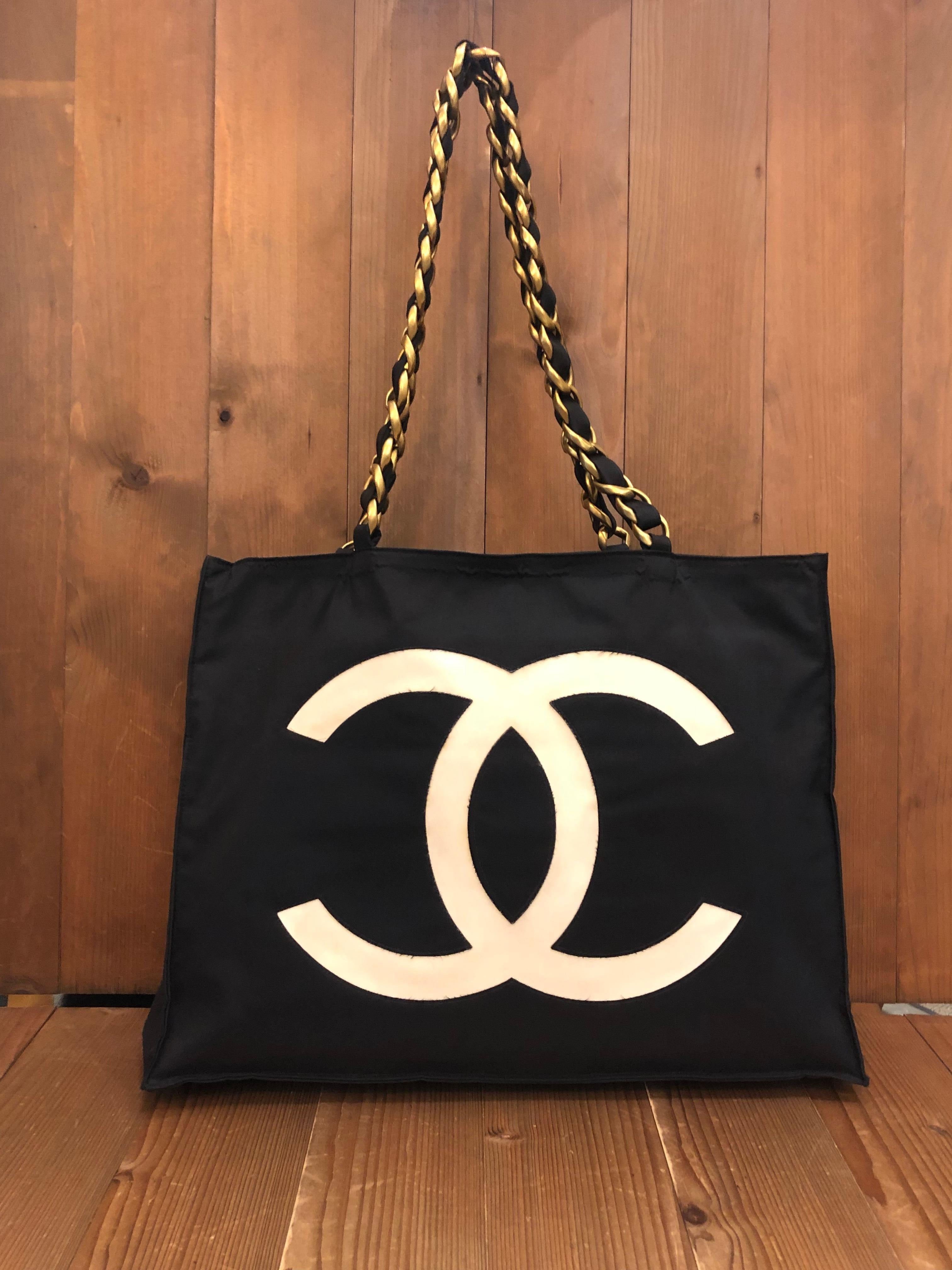 This vintage CHANEL jumbo chain tote is crafted of black nylon featuring a massive cut-out white CC logo on one side and cut-out CHANEL letters on the other. This tote has two sturdy gold toned shoulder chains interlaced with black nylon. The