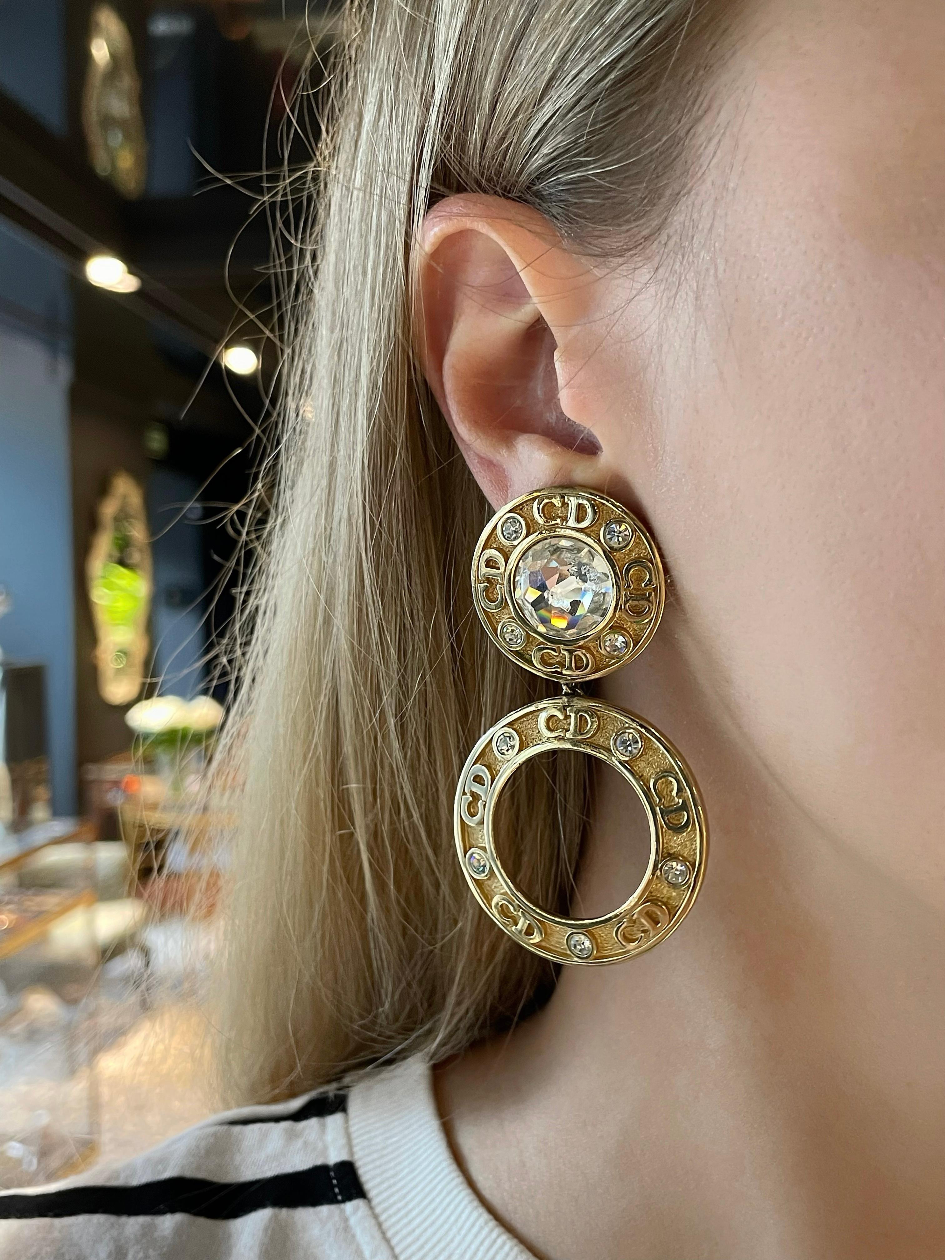 This is a vintage pair of stylish CD logo hoop dangling clip on earrings designed by Christian Dior in 1990’s. The piece is crafted in gold tone base metal and features shiny clear crystals. One central crystal is slightly damaged, but due to the