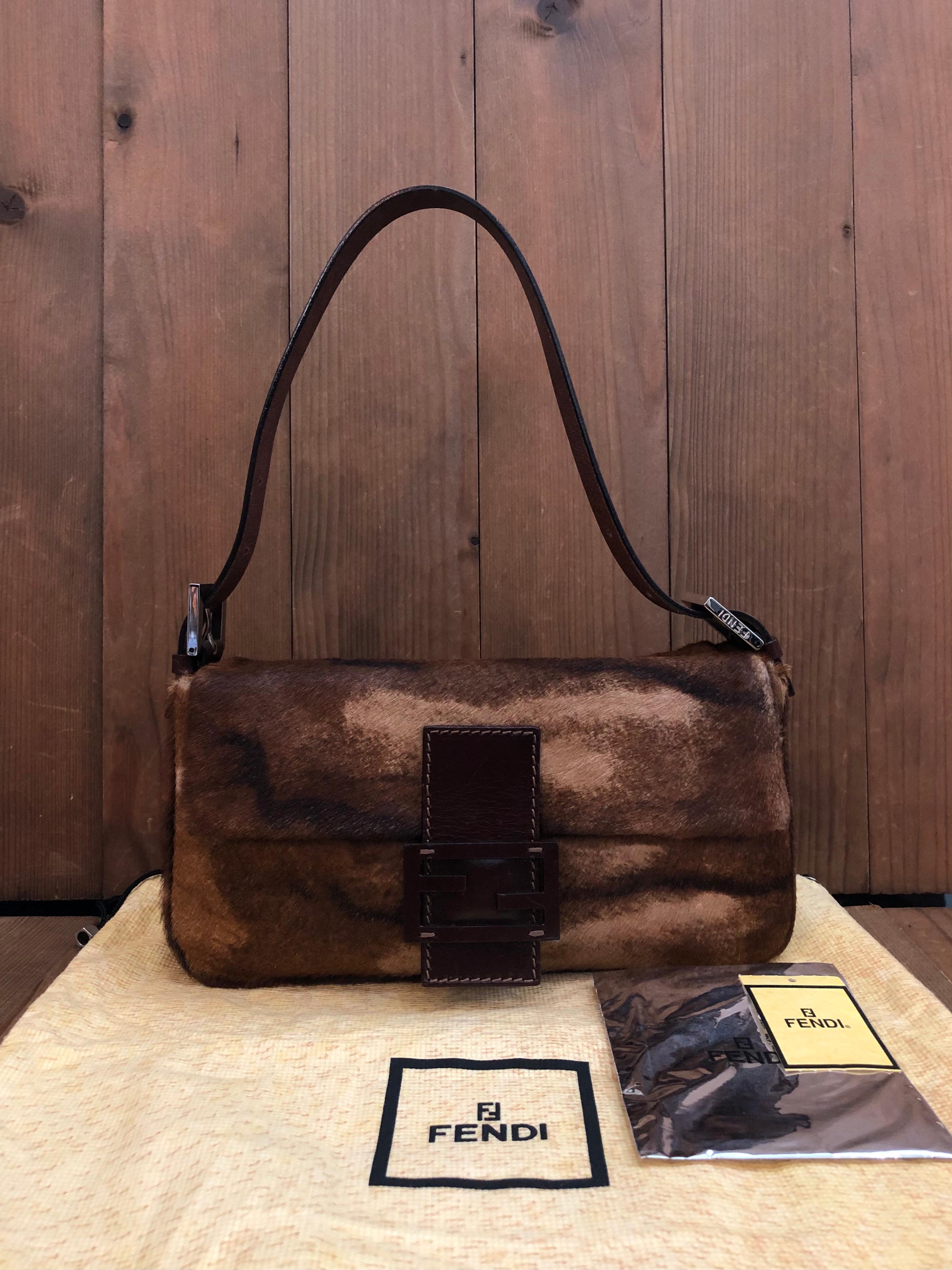 This iconic Fendi Baguette hand bag is crafted of cow leather in brown and beige featuring silver toned hardware. Front leather FF flap magnetic snap closure opens to a brown jacquard interior featuring a zippered pocket. Made in Italy. Measures 10