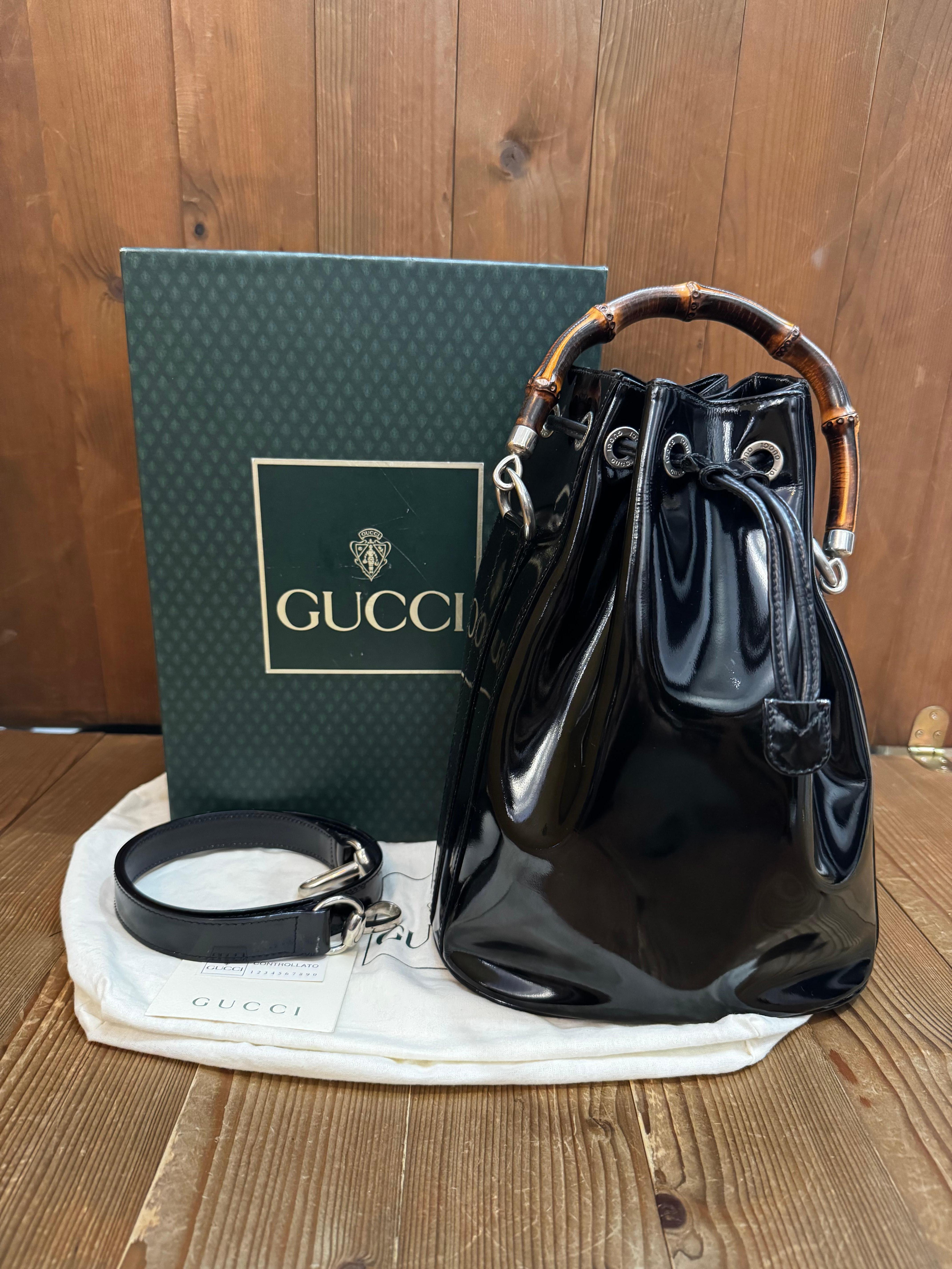 This vintage GUCCI bucket two-way shoulder/top-handled bag is crafted of patent cow leather in black featuring silver-toned hardware and a sturdy bamboo handle. Top drawstring closure opens to a leather interior featuring a zippered pocket. Made in