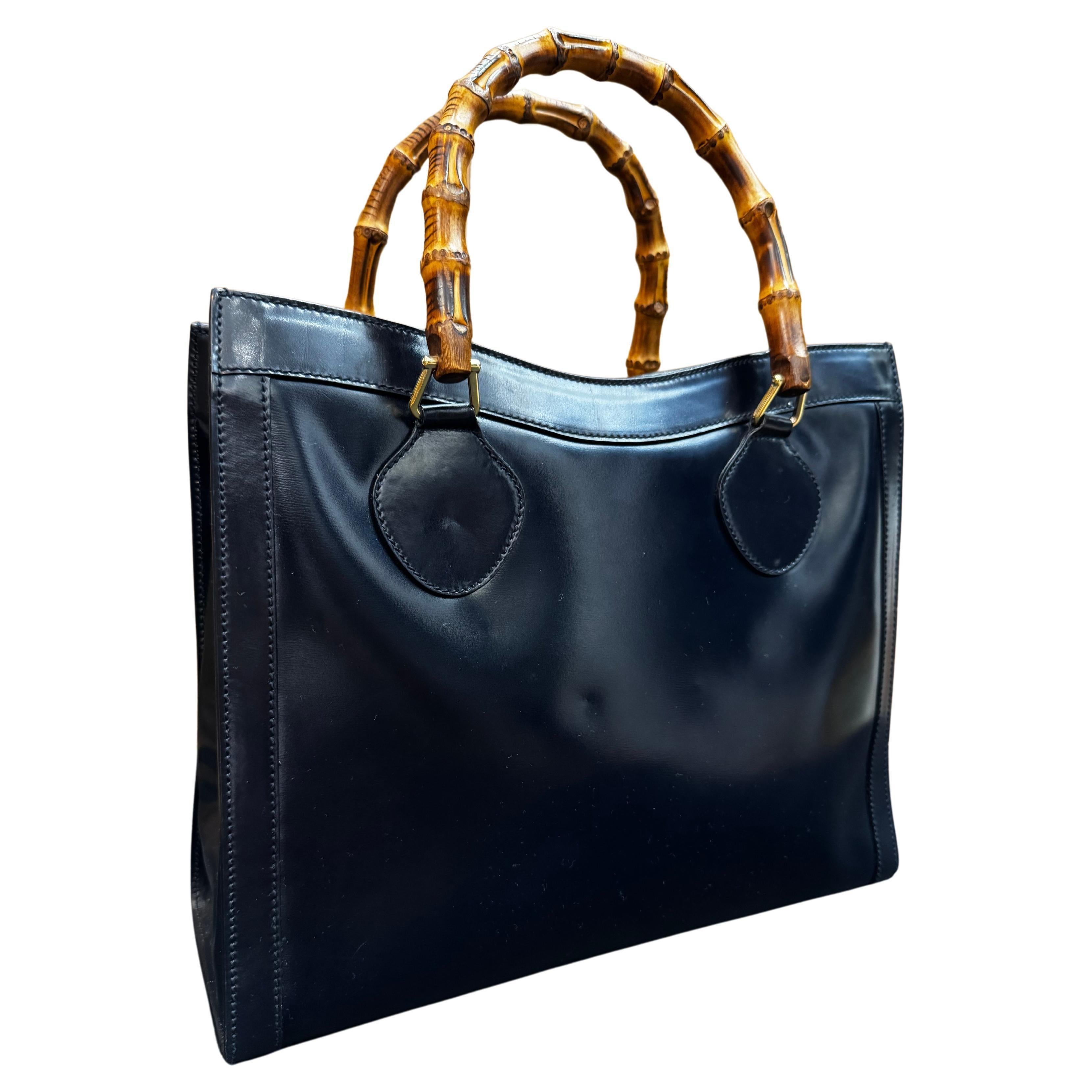 This vintage GUCCI Diana bamboo tote is crafted of polished calfskin leather in dark navy featuring gold toned hardware and sturdy bamboo handles. Top magnetic snap closure opens to a diamanté jacquard interior featuring two main compartments and