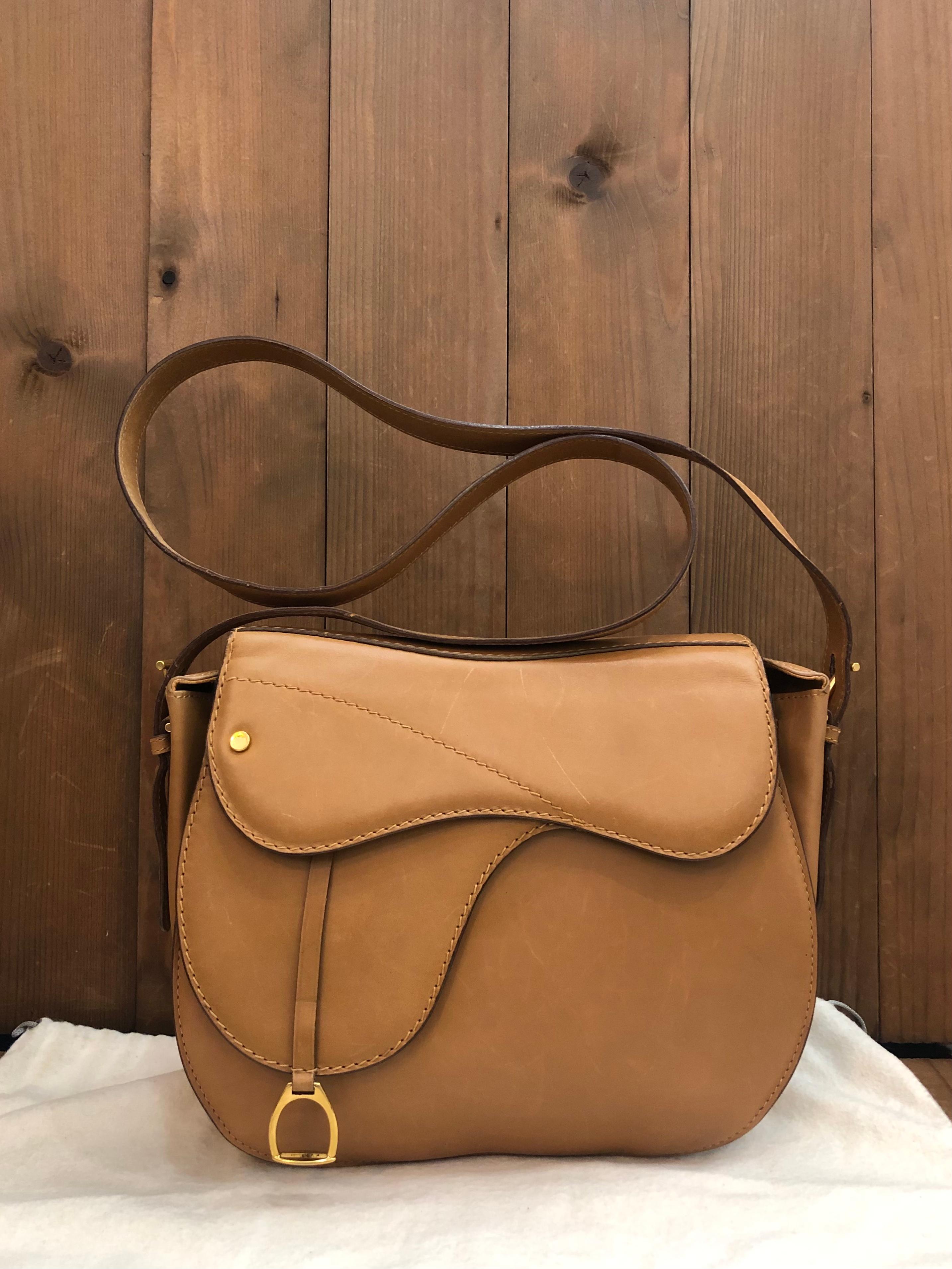 This 1990s vintage GUCCI saddle bag is crafted of smooth calfskin leather in camel featuring gold toned hardware. Front magnetic snap closure opens to a leather interior featuring a zippered pocket. Made in Italy. Measures approximately 9 x 9 x 3