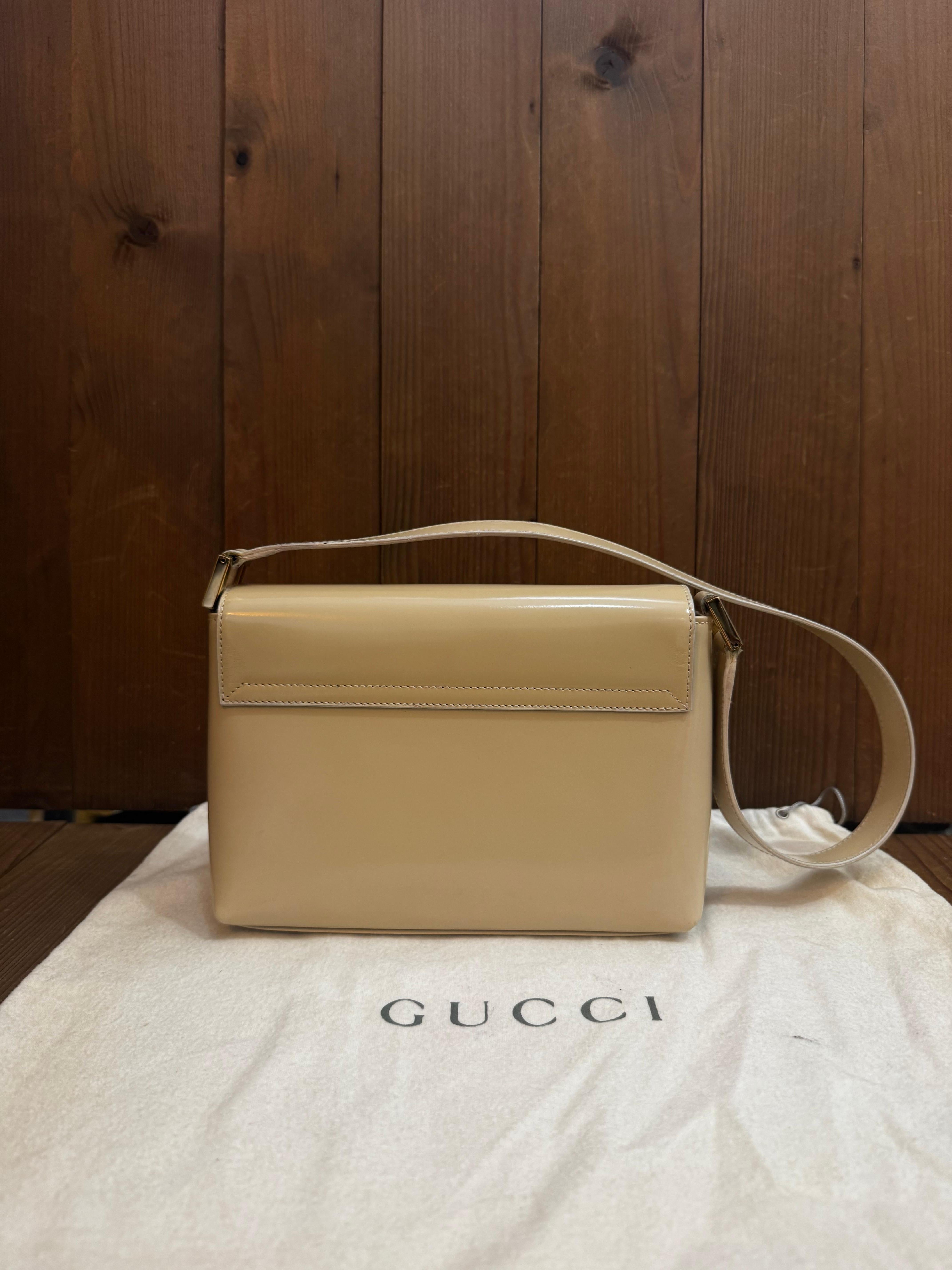 Este bolso bandolera vintage de GUCCI está confeccionado en piel de becerro pulida de color beige con un borde metálico dorado alrededor de la solapa. La solapa frontal con cierre magnético a presión se abre a un interior revestido que ha sido