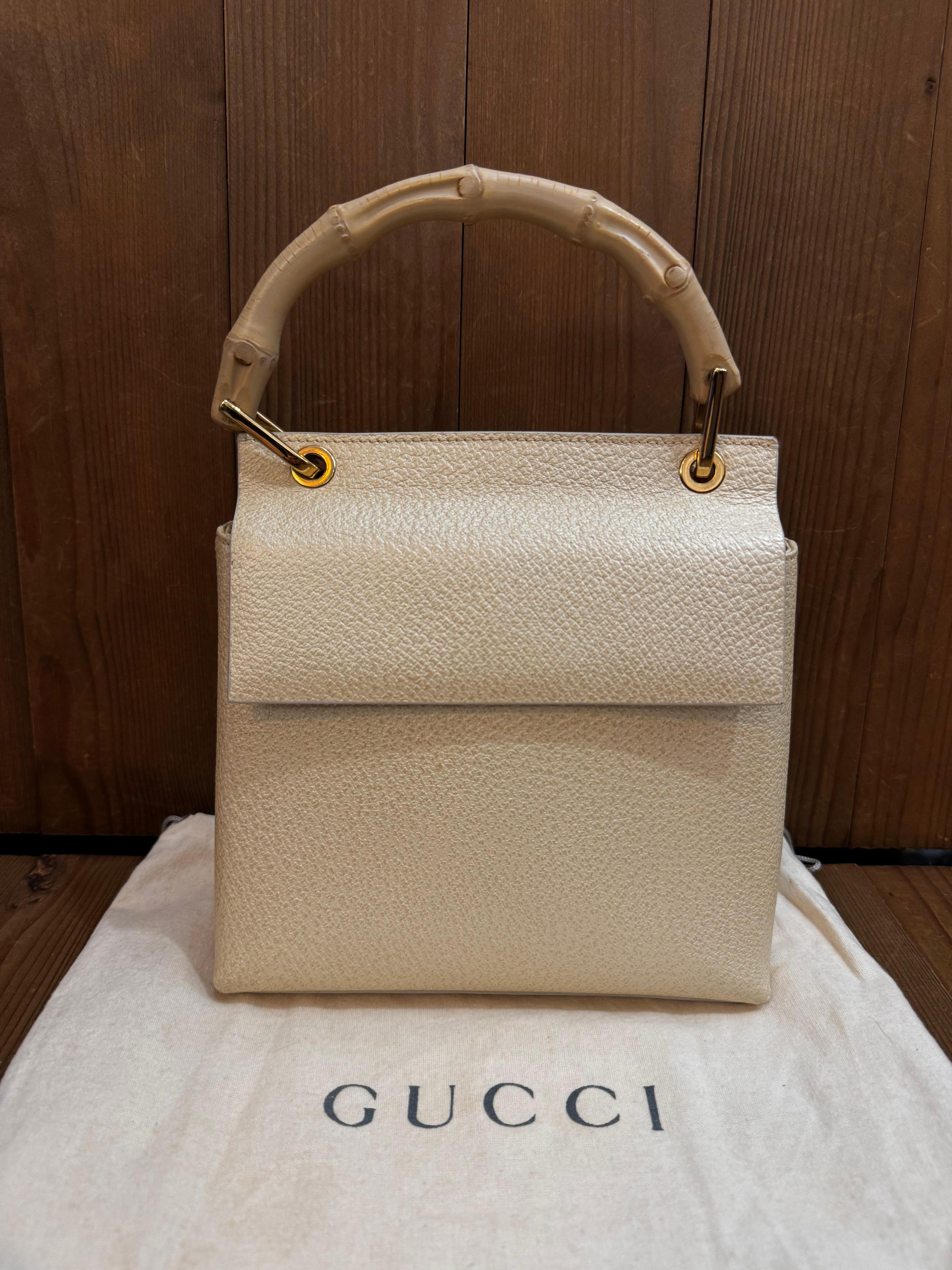 This vintage GUCCI small bamboo top handle bag is crafted of pigskin leather in a pearlywhite hue featuring gold toned hardware and a bamboo handle. Front flap magnetic snap closure opens to a nubuck leather interior in beige featuring a zippered