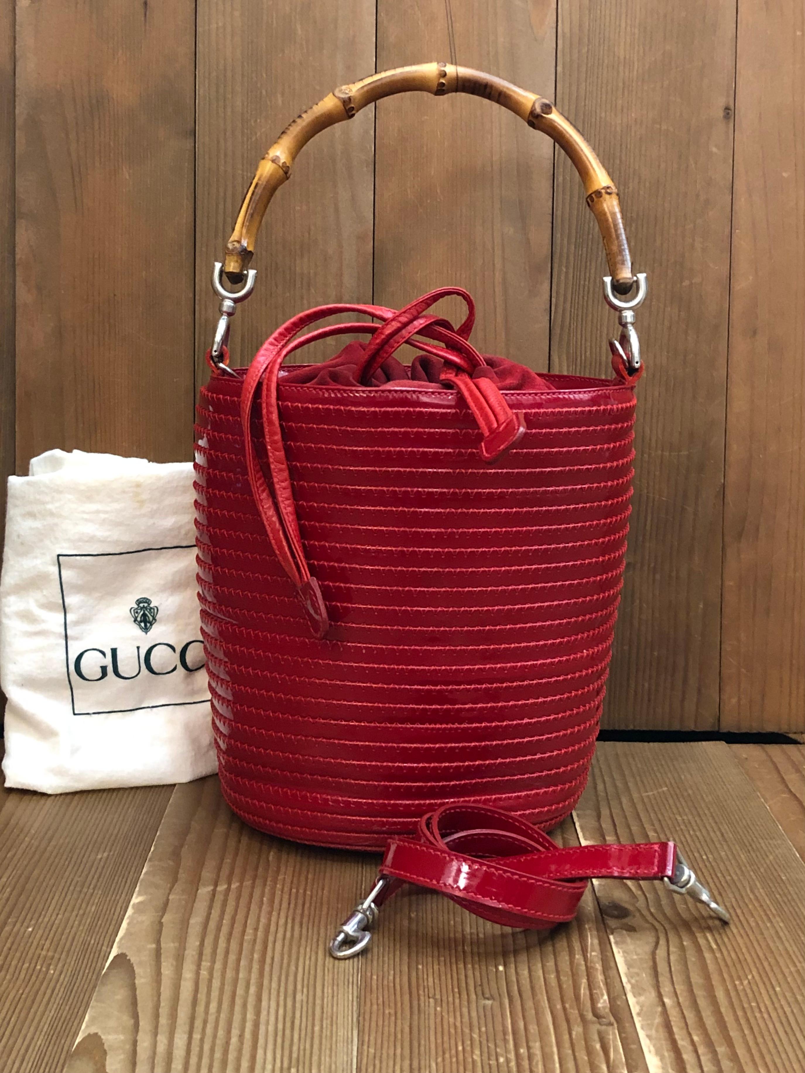 This vintage GUCCI bucket shoulder bag is crafted of red patent leather in folds featuring silver toned hardware and a bamboo handle. Top drawstring in nubuck leather closure opens to a beige leather interior featuring a zippered pocket. Made in