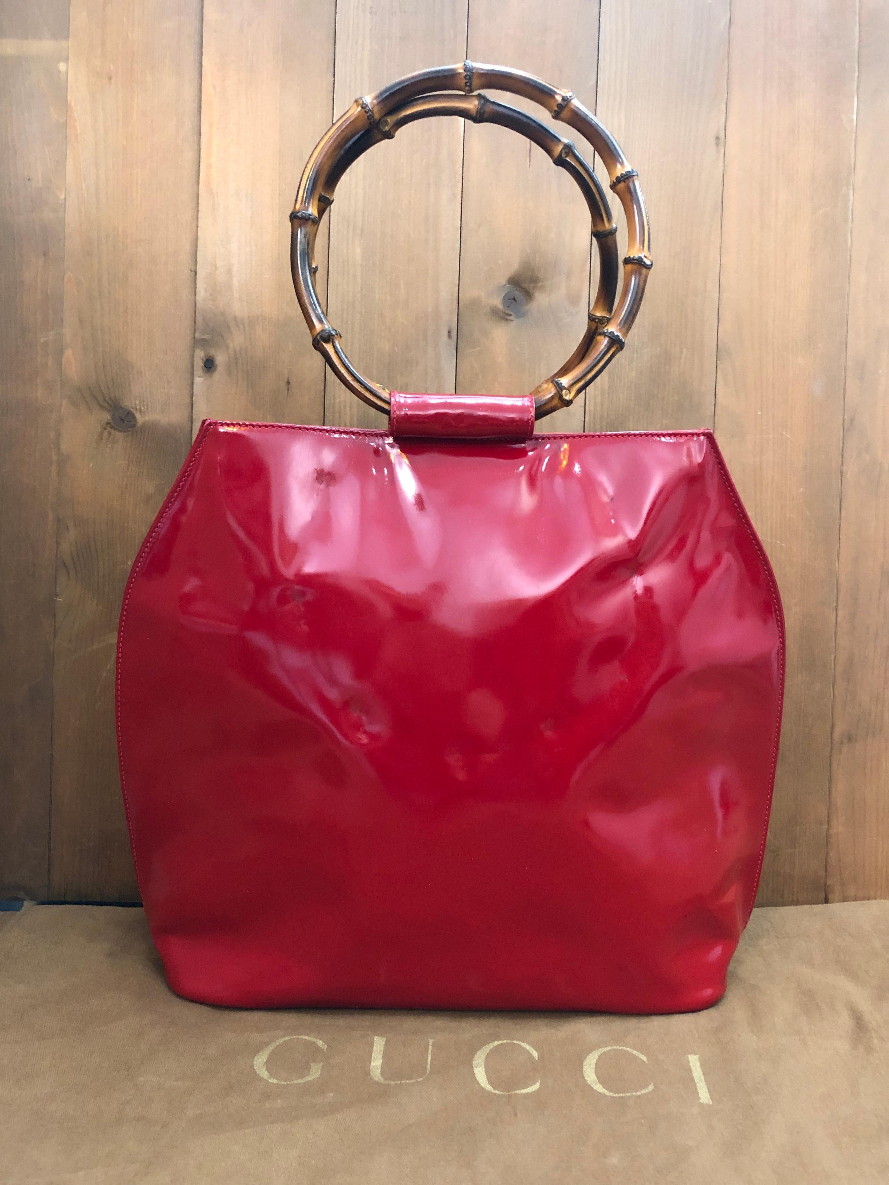 This vintage GUCCI top handle shoulder tote bag is crafted of patent leather in red featuring two massive bamboo ring handles. Top magnetic snap closure opens to a new interior in beige featuring a zippered pocket. Made in Italy. Measures