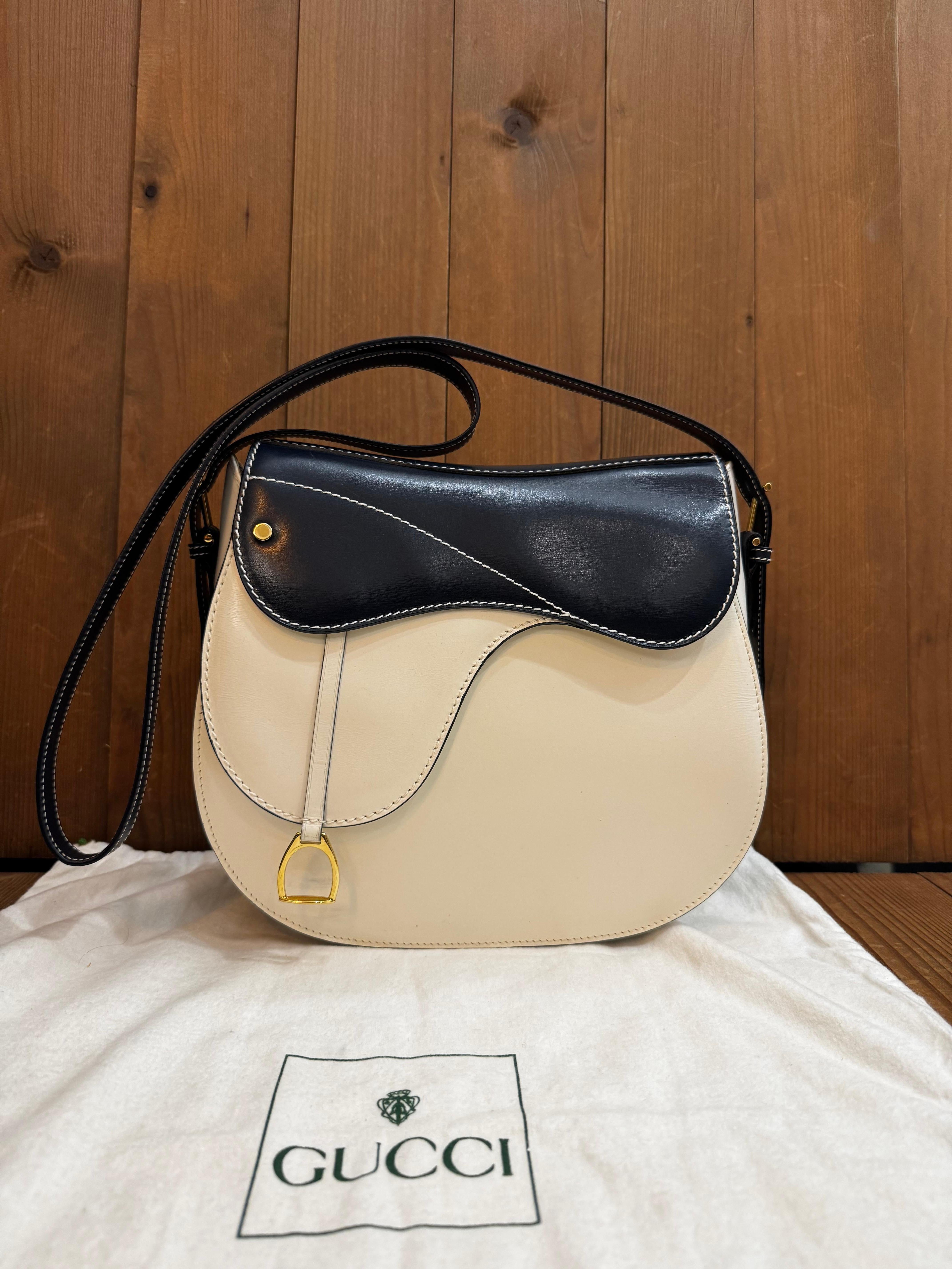 This beautiful vintage GUCCI two-toned saddle bag is crafted of smooth calfskin leather in off-white and navy featuring gold toned hardware. Front magnetic snap closure decorated with a stirrup charm opens to a beige leather interior with a zippered