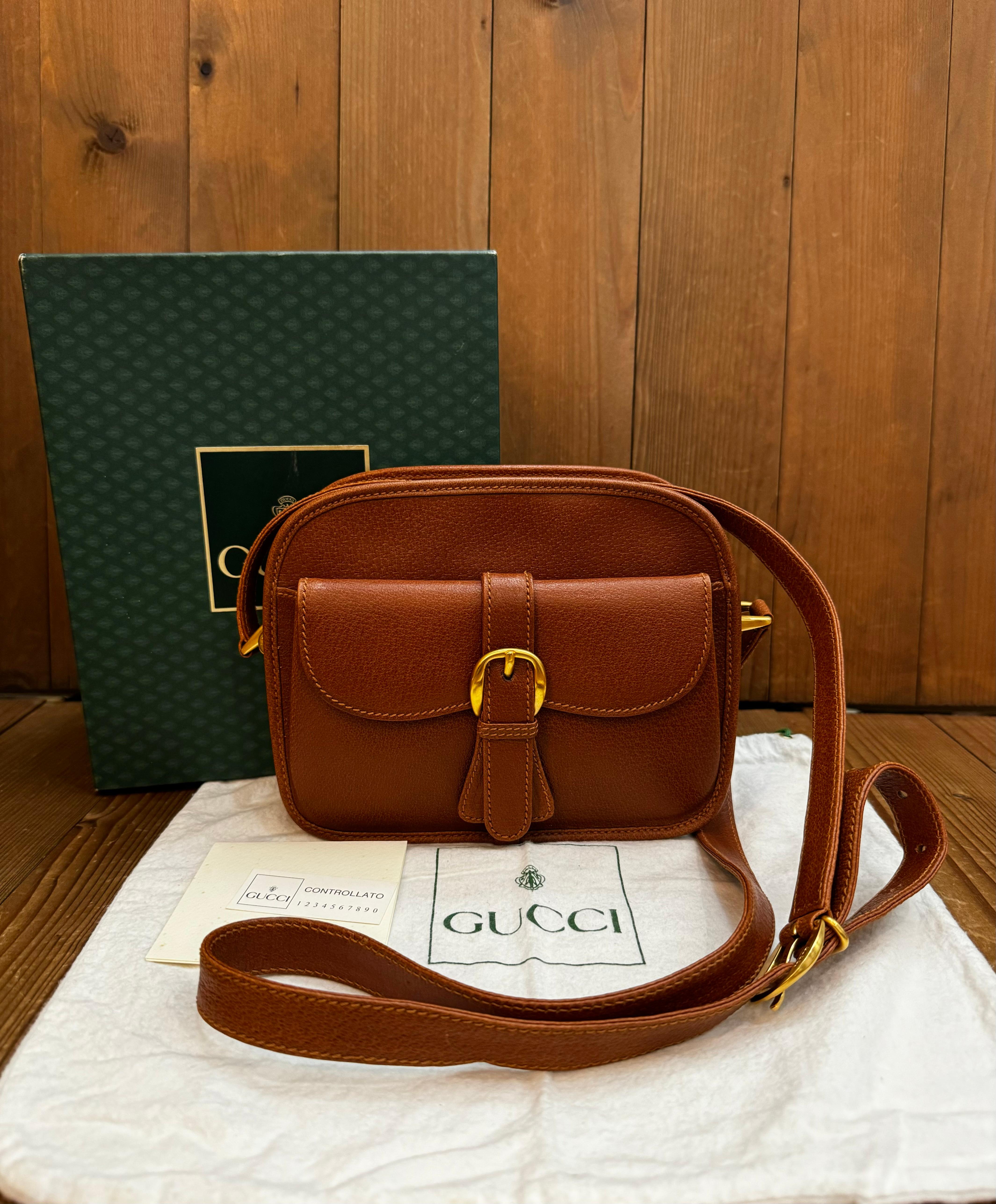 This vintage GUCCI Web camera crossbody bag is crafted of pigskin leather in caramel featuring brushed gold toned hardware decorated with a red/green stripe along the sides and bottom. Top zipper closure opens to a jacquard inteior featuring a patch