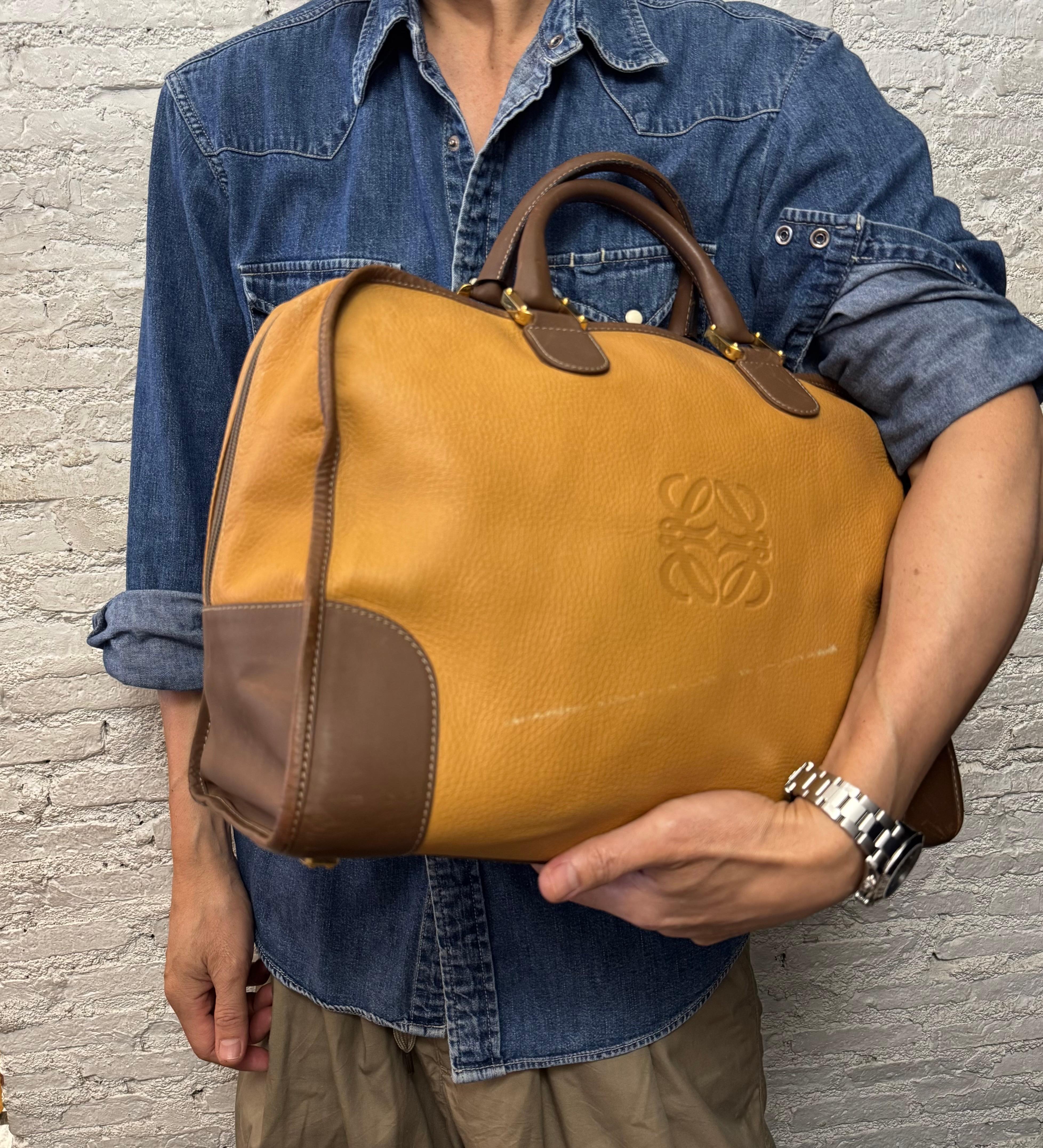 Diese LOEWE Amazona Boston Tasche im Vintage-Stil ist aus grob genarbtem Kalbsleder in Senfgelb gefertigt und mit glattem Kalbsleder in Braun eingefasst. Sie verfügt über goldfarbene Beschläge und gerollte Ledergriffe. Der Reißverschluss an der