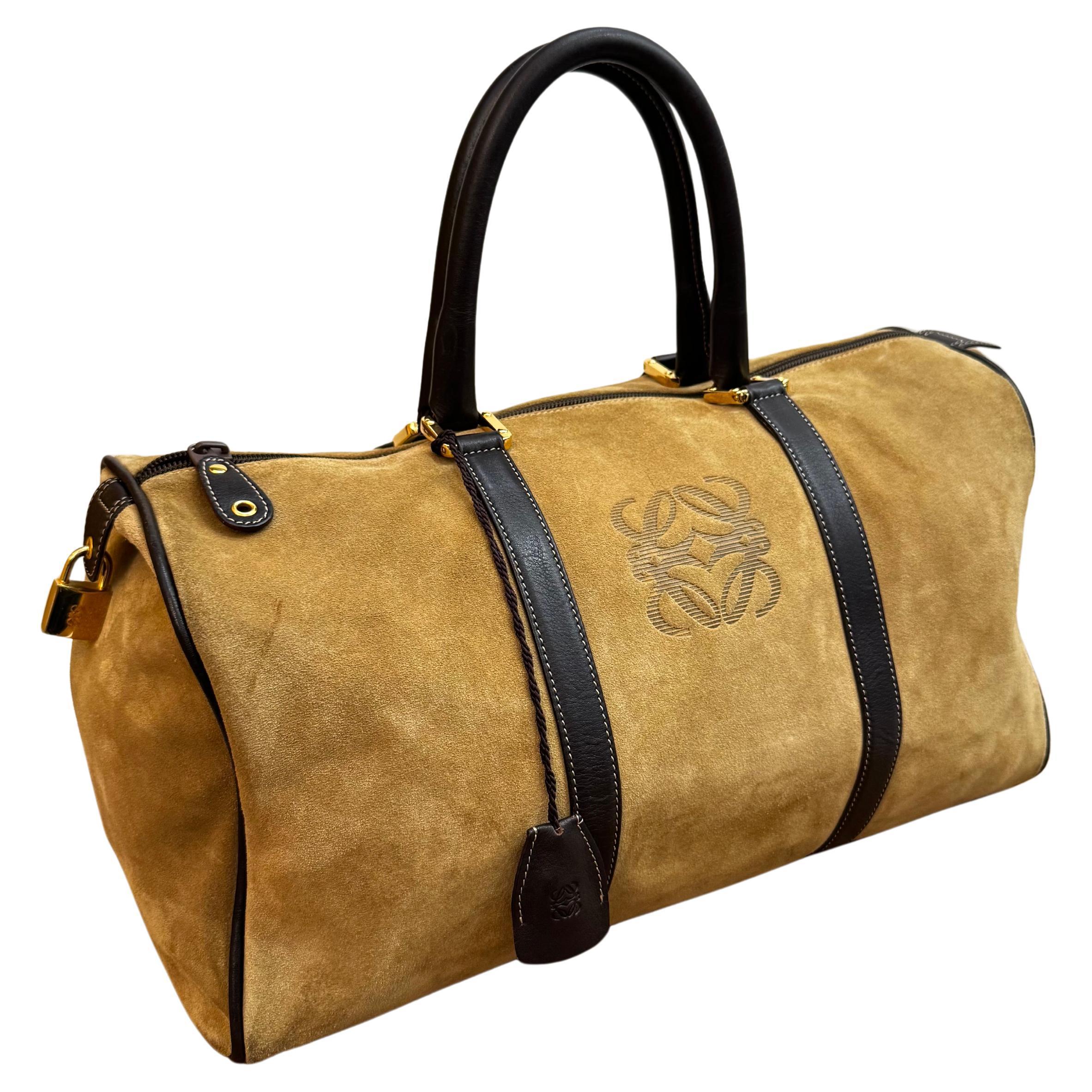 Ce sac vintage LOEWE Anagram boston est confectionné en daim de veau bordé de cuir de veau lisse de couleur marron et doté de ferrures dorées. Les poignées en cuir roulées se posent confortablement sur l'épaule. La fermeture à glissière sur le