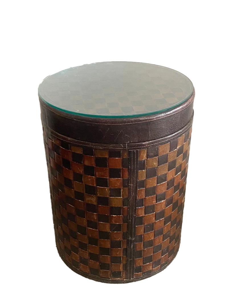 Esta mesa auxiliar de piel tejida y madera tiene almacenaje interior y tablero de cristal. Es uno de los muebles más sorprendentes que he visto. El cristal lo hace perfecto para tomar copas junto a un sofá y, así, no dañar el cuero. El interior está