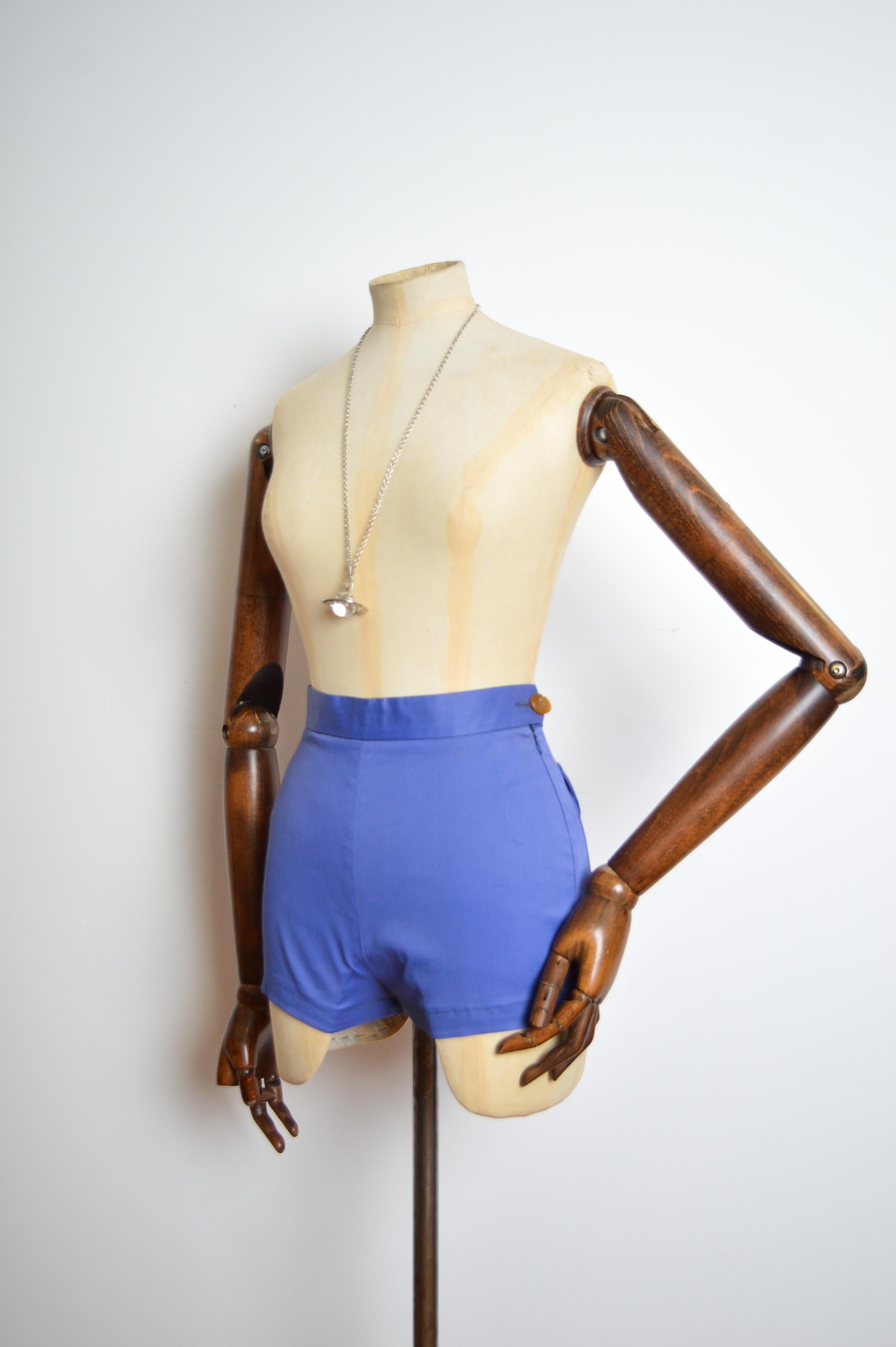 Hoch taillierte Vivienne Westwood Booty Shorts in Kornblumenblau mit Taschen auf dem Gesäß mit Kugelknöpfen sowie Kugelknopf an der Hüfte und verdecktem Seitenreißverschluss.
Steigung; 13
