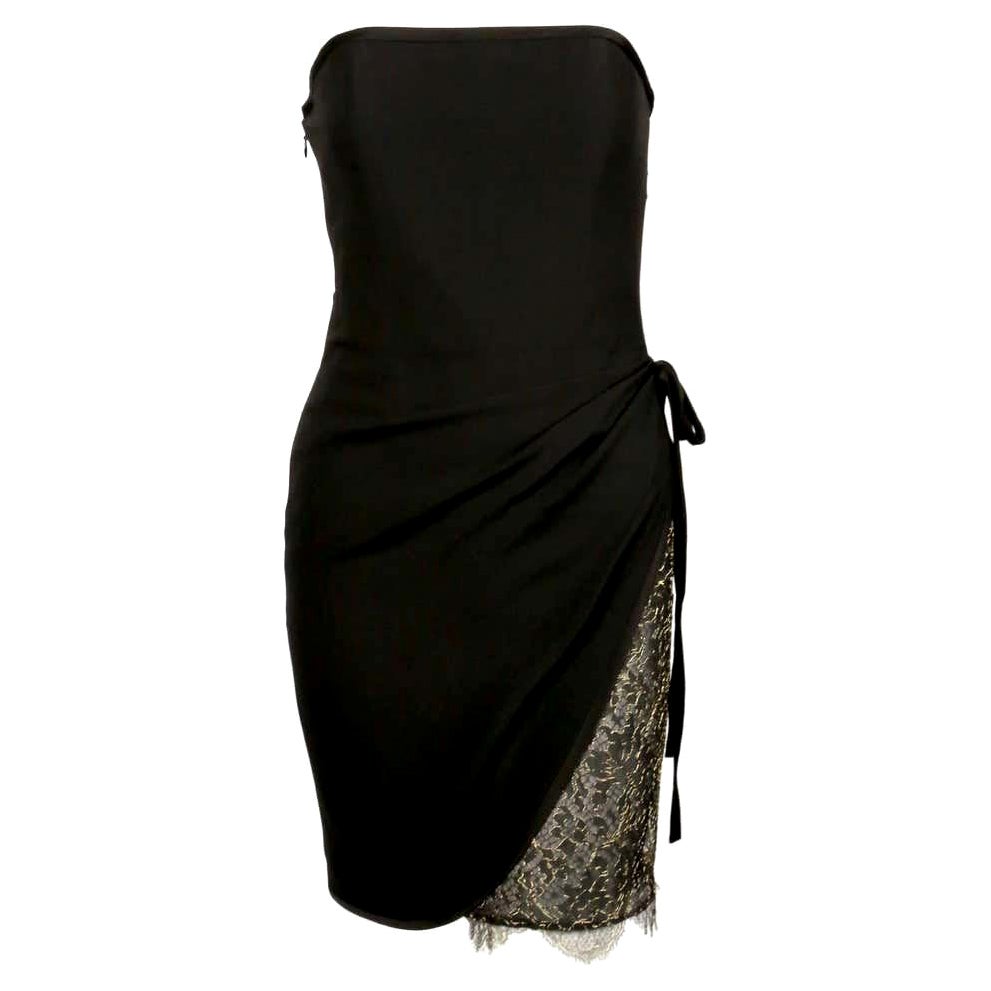 Trägerloses Cocktailkleid von Yves Saint Laurent aus den 1990er Jahren. Das Kleid in Schwarz hat eine asymmetrische Wickelvorderseite, die an der Hüfte gebunden wird, und zeigt einen Einsatz aus goldfarbener Metallic-Spitze, der auch unter den Saum