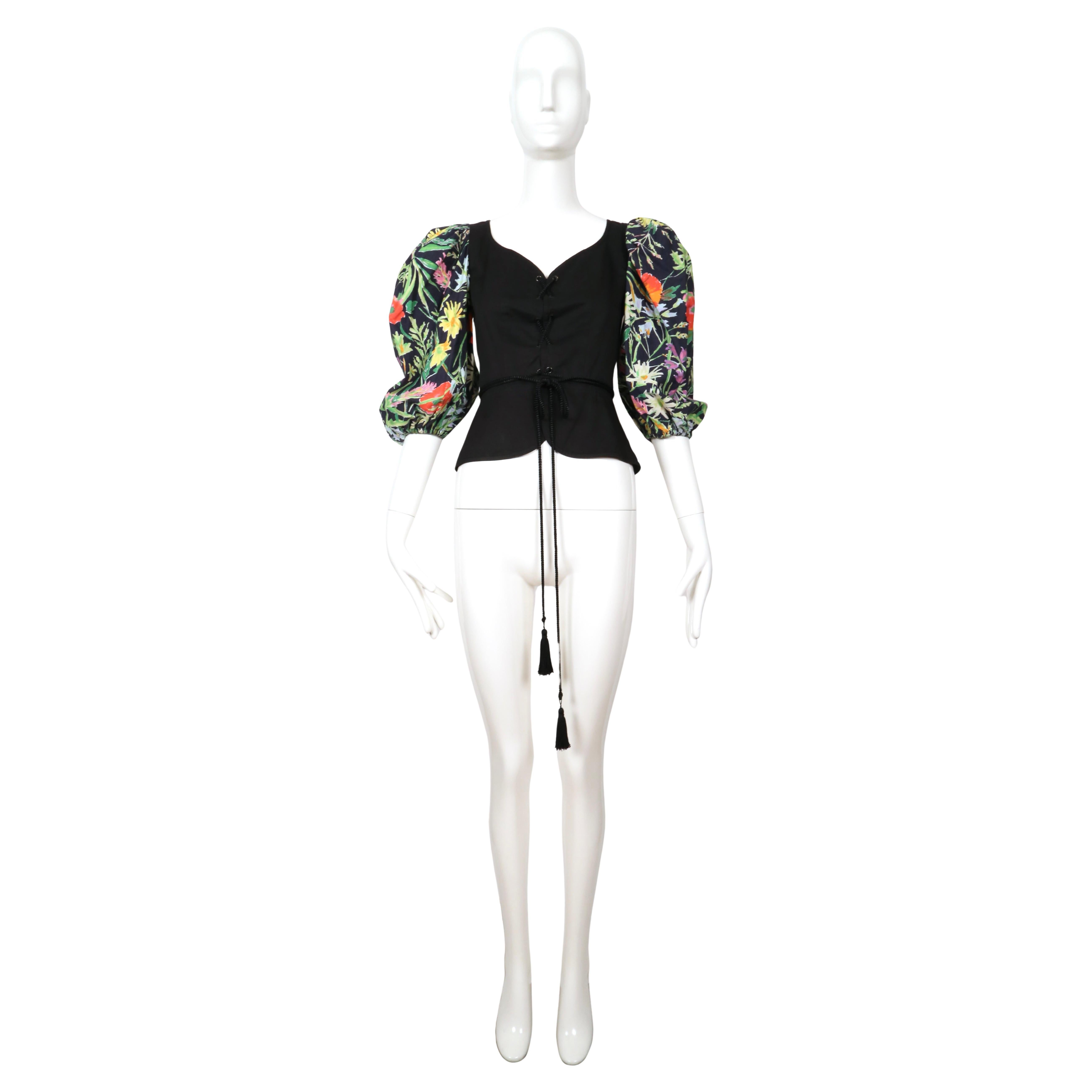 Black cotton lace up corset top with metal grommets and full floral printed sleeves designed by Yves Saint Laurent dating to the 1990's for the 'variation' diffusion line. Labeled a French size 38. Approximate measurements with fabric touching: