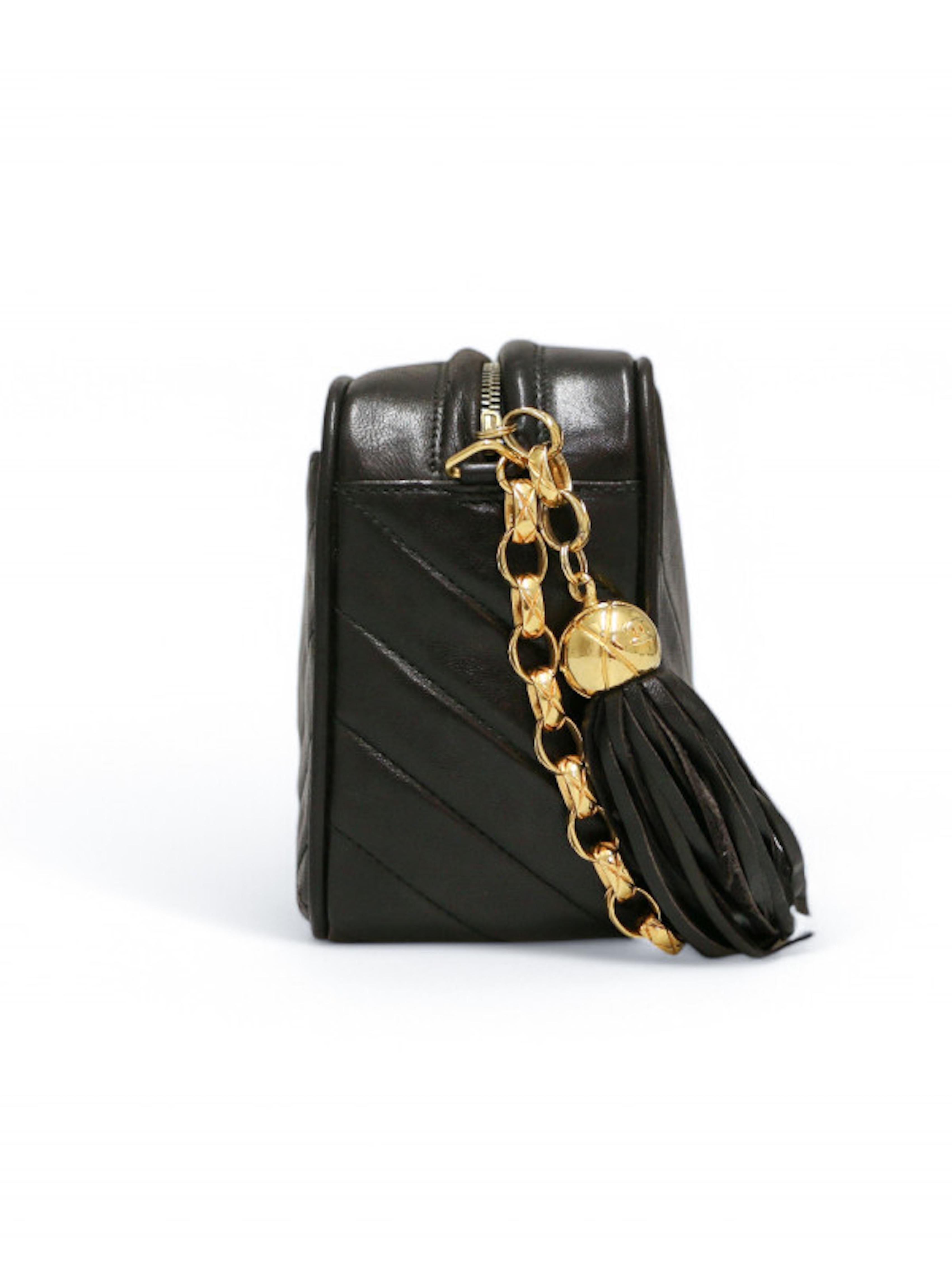 Mini Caméra Vintage CHANEL en cuir d'agneau noir à chevrons livrée dans un dustbag CHANEL.
Petit sac avec chaîne à bijoux plaquée or et pompon frangé en cuir. Grande poche intérieure et deux plus petites, dont l'une est zippée
Condit : très