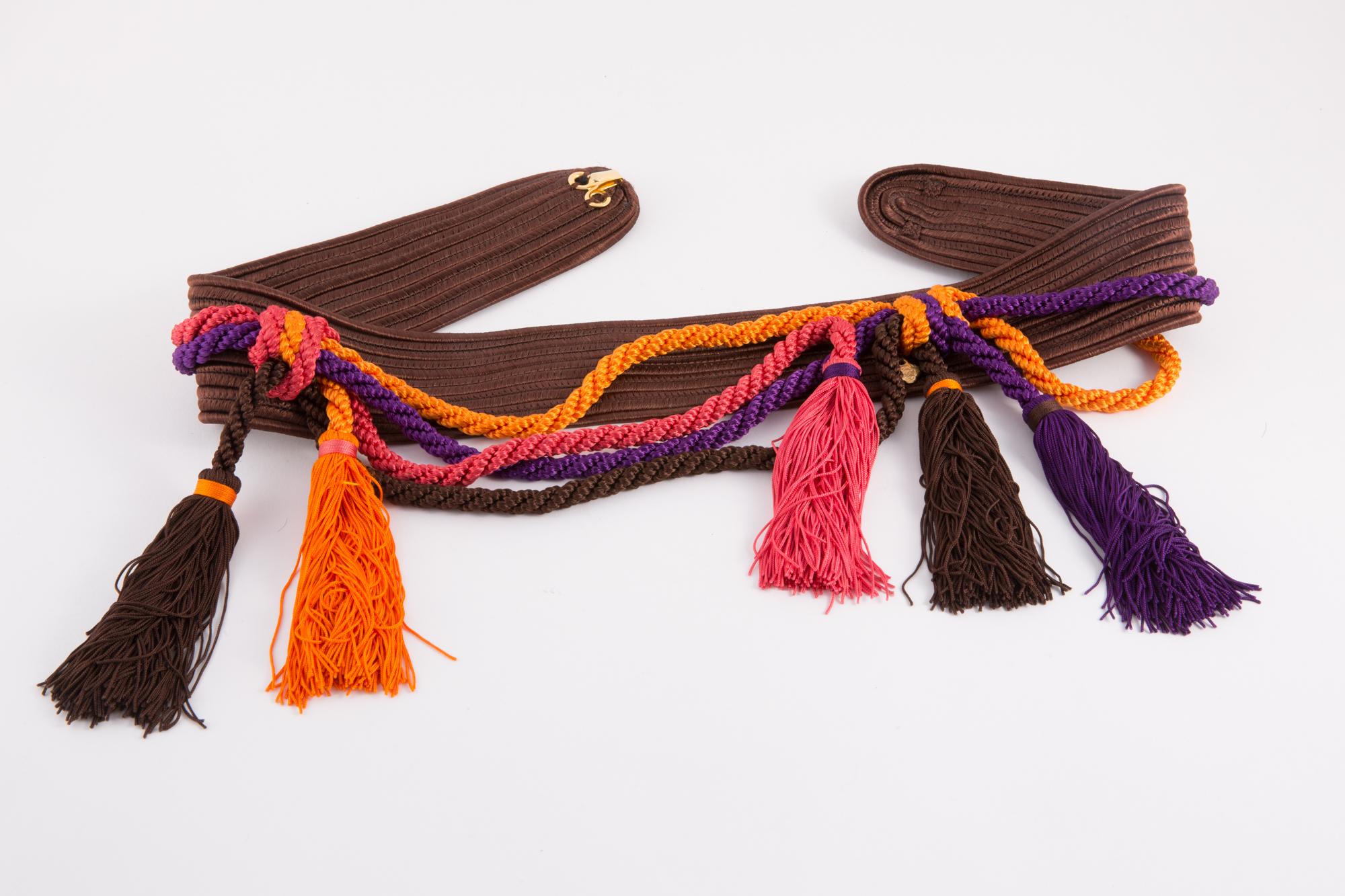 Multicolor Yves Saint Laurent braided belt featuring brown braided belt, and purple & orange fringed pompons, logo gold tone metallic plaque. See catwalk 1991s photo.
In excellent vintage condition. Made in France. 
Maxi Length 31.4in. (80cm)
Width