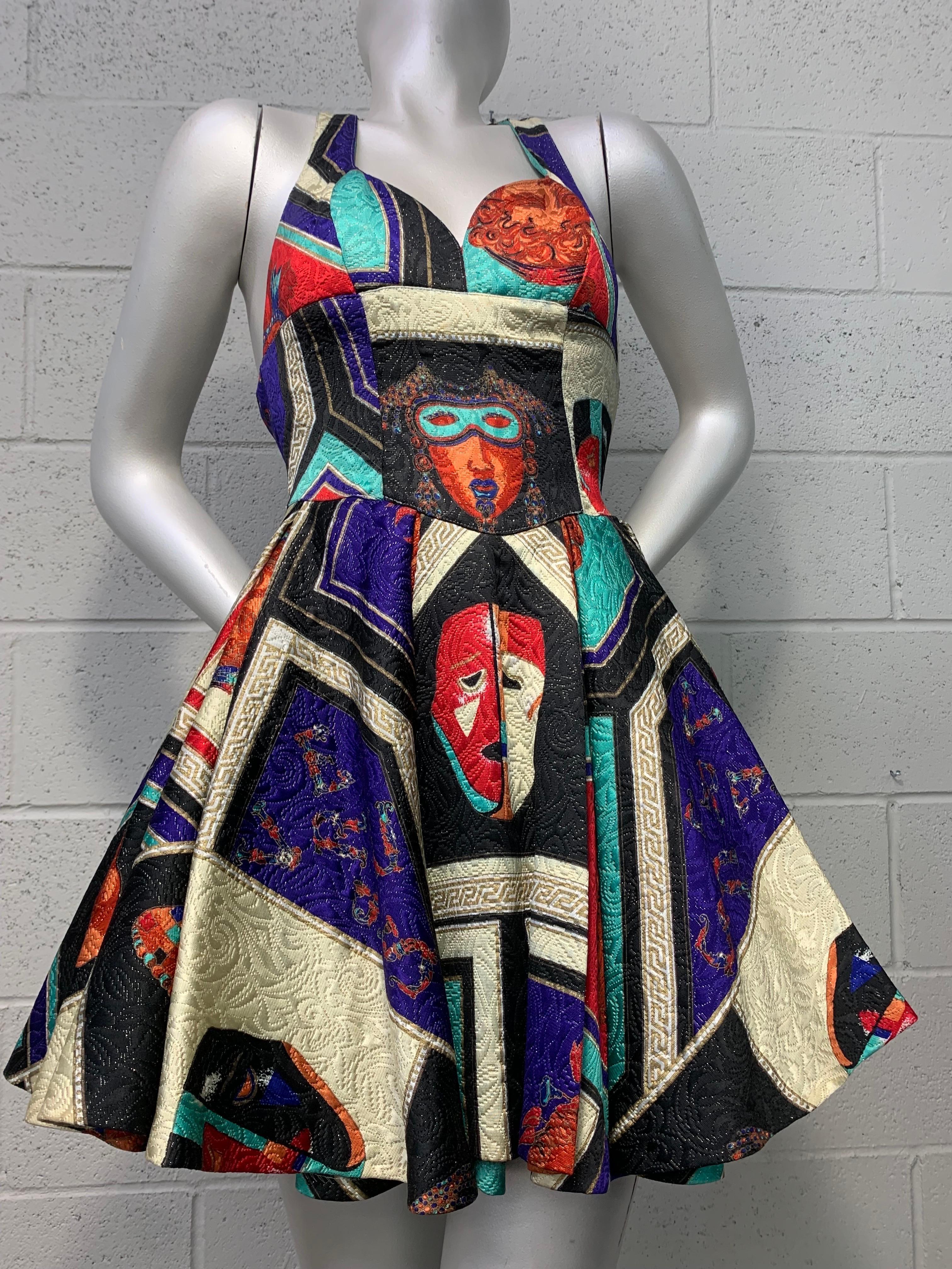 A 1992 Versus by Gianni Versace 1950s and masquerade-inspired matelissé silk lamé fit and flare mini dress with gold lamé tulle crinoline under-skirt. Bold graphic mask imagery paired with arresting geometrics and color-blocking give this piece a